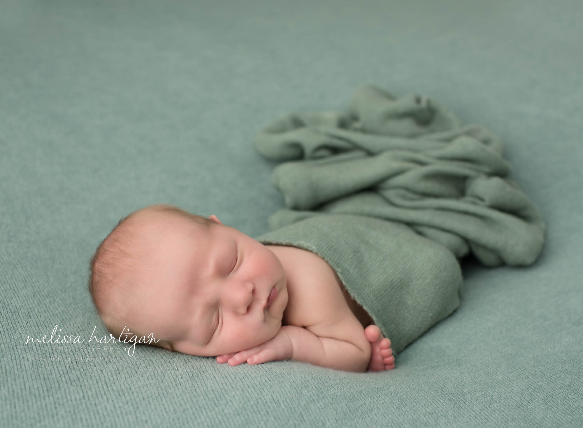 newborn baby boy pose don tummy with green layer draped over back CT newborn photoshoot