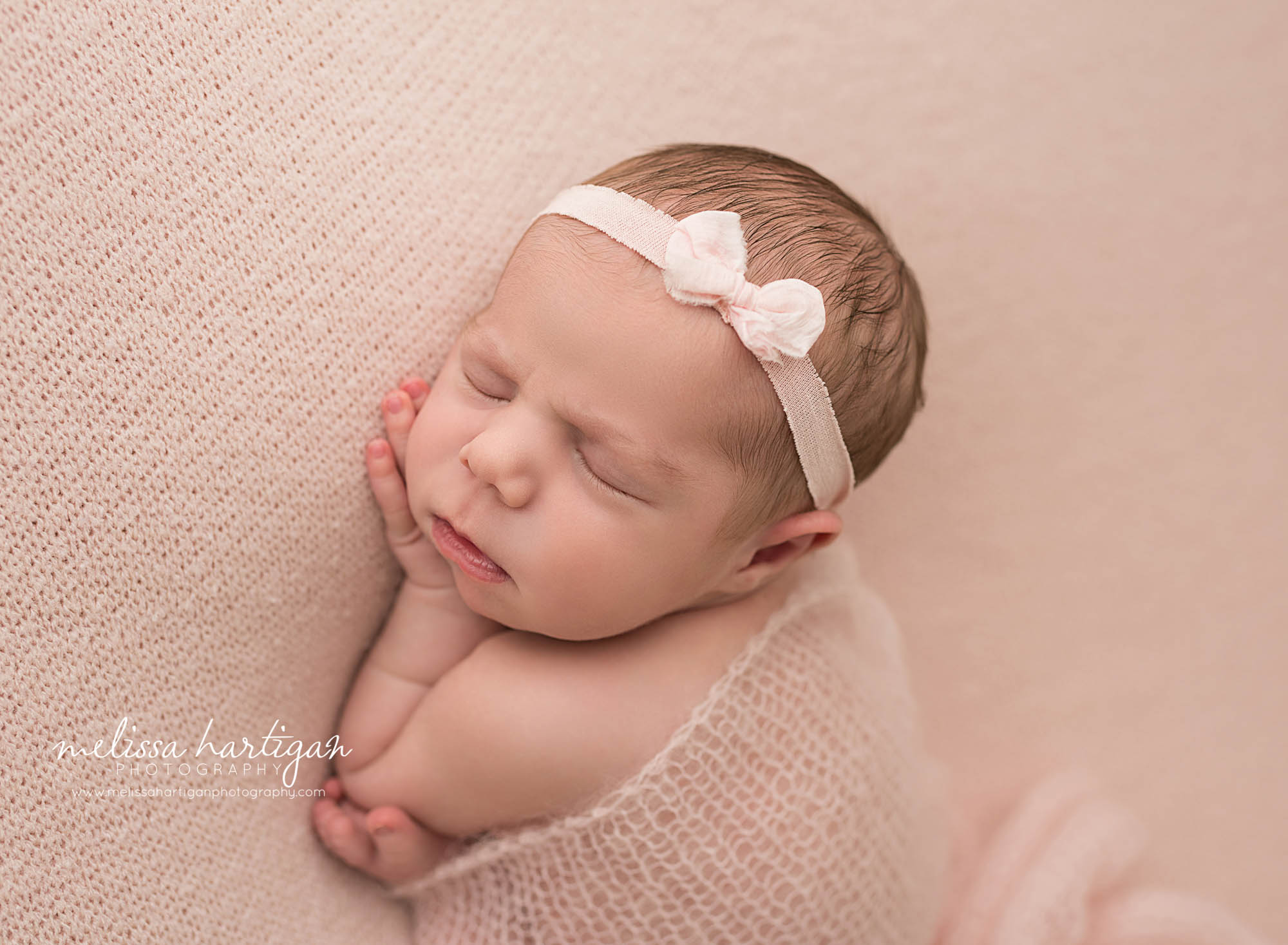 newborn baby girl posed on side on pink backdrop wearing pink bow headband