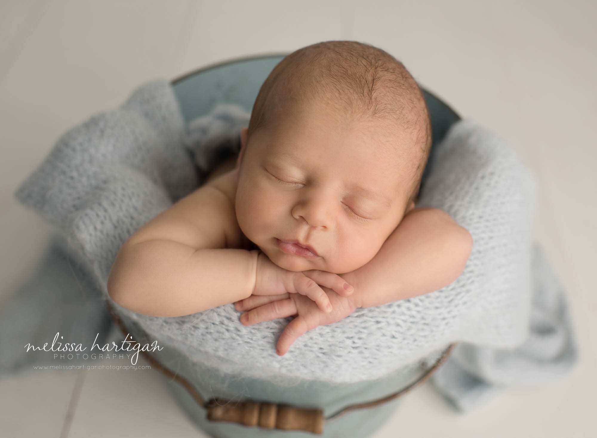 newborn baby boy posed in bucket with light blue knitted layer wrap