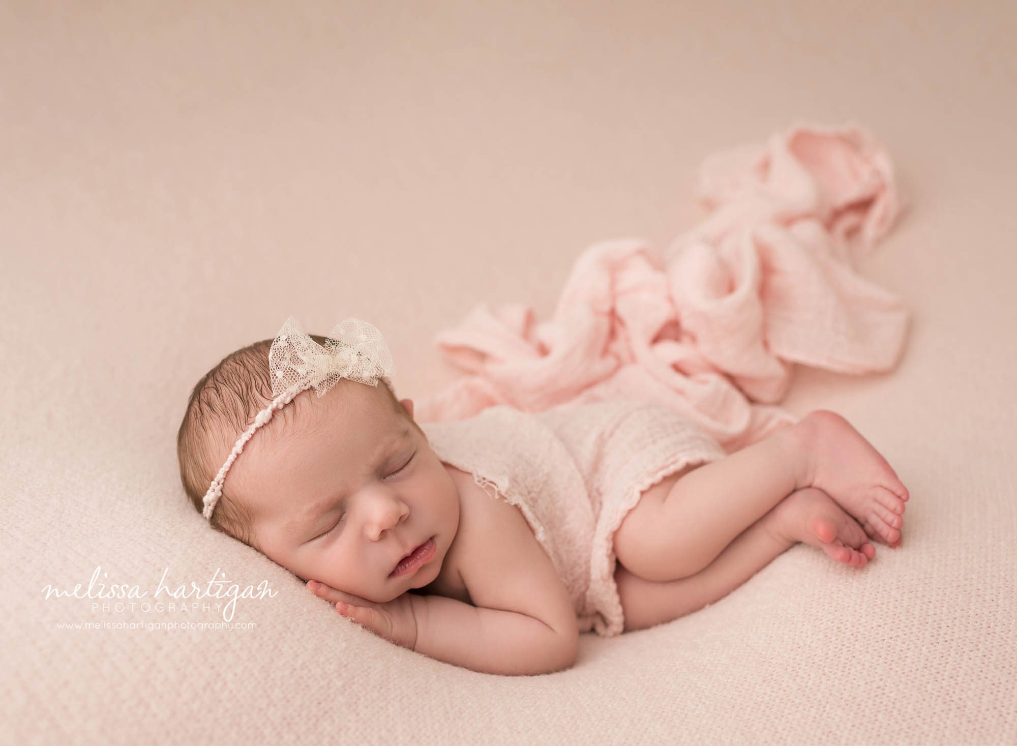 newborn baby girl pose don side on pink backdrop with pink layer wearing pink bow headband newborn photography shelton ct