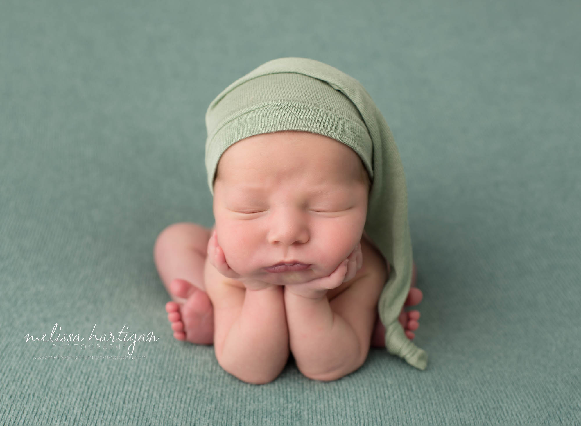 newborn baby boy posed froggy pose wearing green sleepy cap pose don sage green backdrop newborn photography east lyme