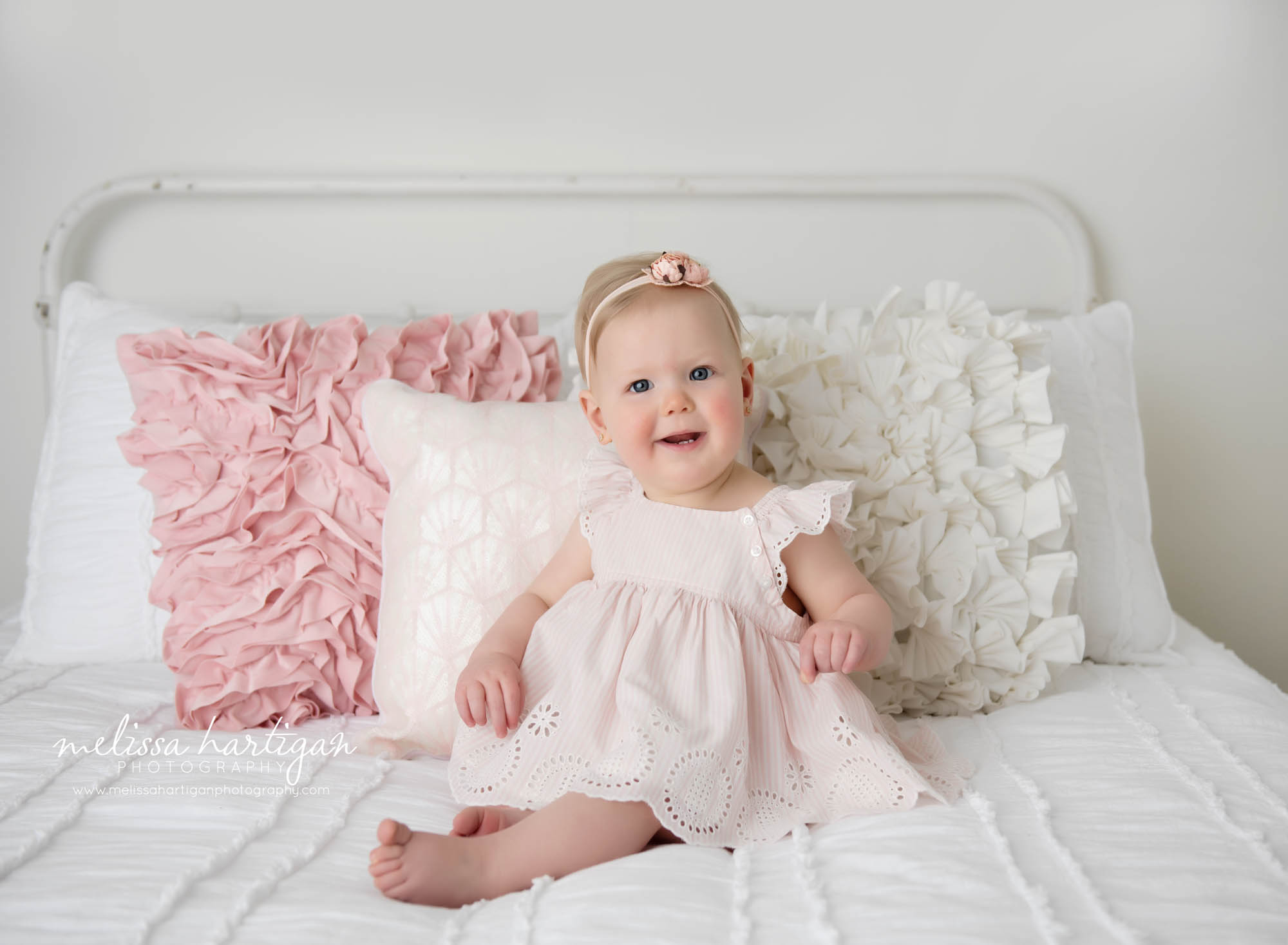 baby girl sitting on bed at one years old wearing dress