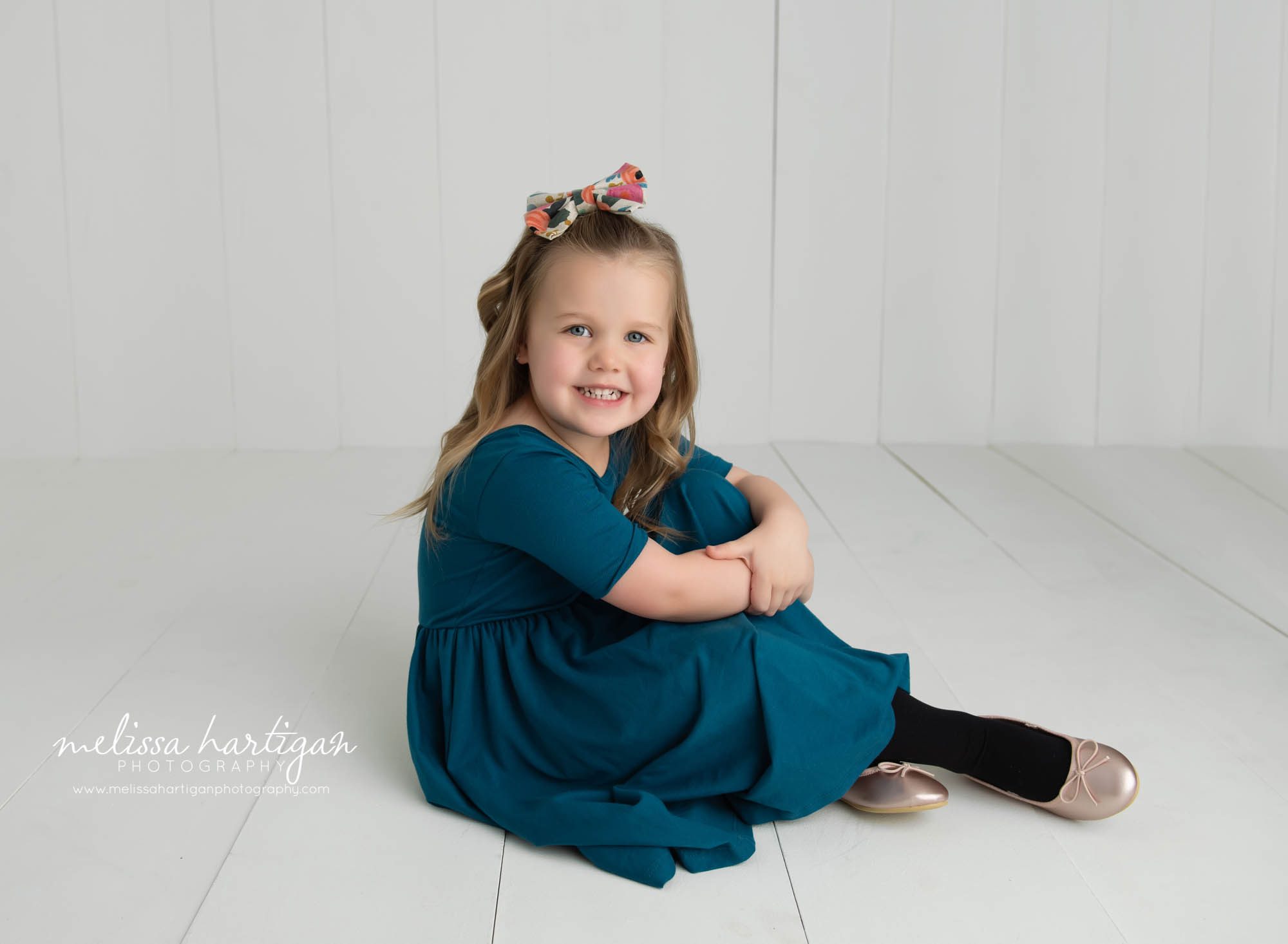 big sister sitting on floor in photography studio smiling for a pose CT childrens photorgaphy