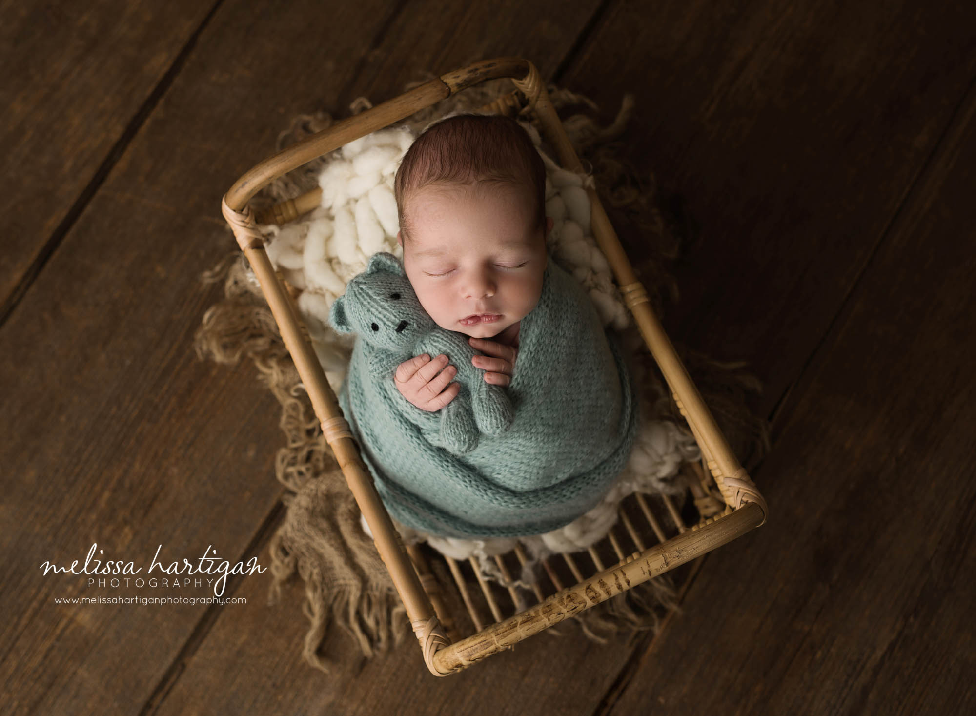 newborn baby boy swaddled in green knitted wrap holding sage green knitted teddy bear posed in basket newborn photography coventry ct