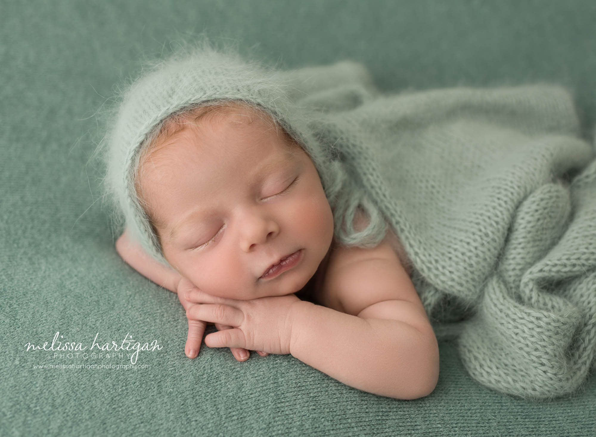 newborn baby boy posed on tummy with cheek resting on top of hands wearing knitted sage green angora bonnet coventry CT newborn photography