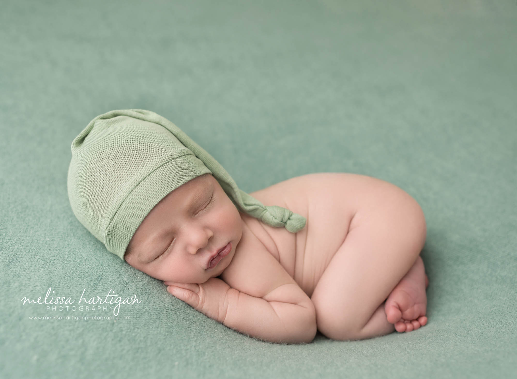 newborn baby boy posed on sage green backdrop wearing sleepy cap newborn photorgrapher CT