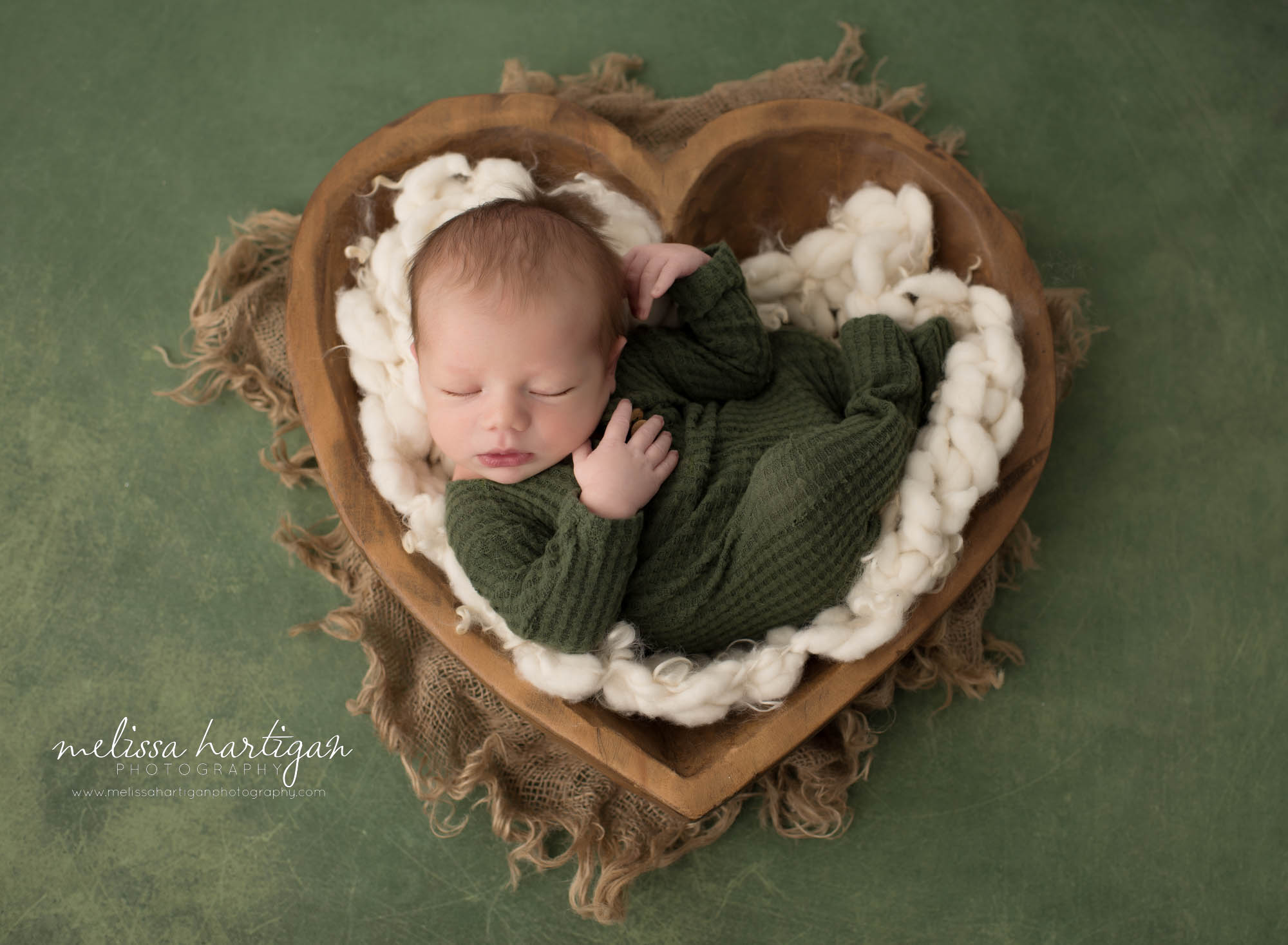 newborn baby boy posed in wooden heart bowl prop wearing green waffle footed sleeper CT newborn photography