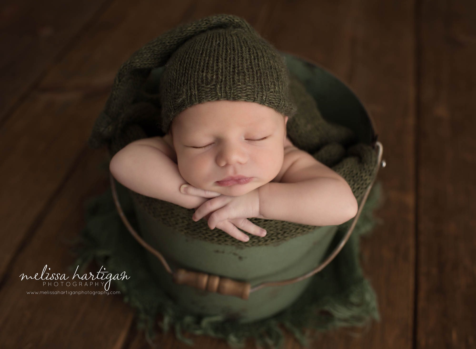 newborn baby boy posed in green metal bucket wearing green knitted sleepy cap newborn photography CT