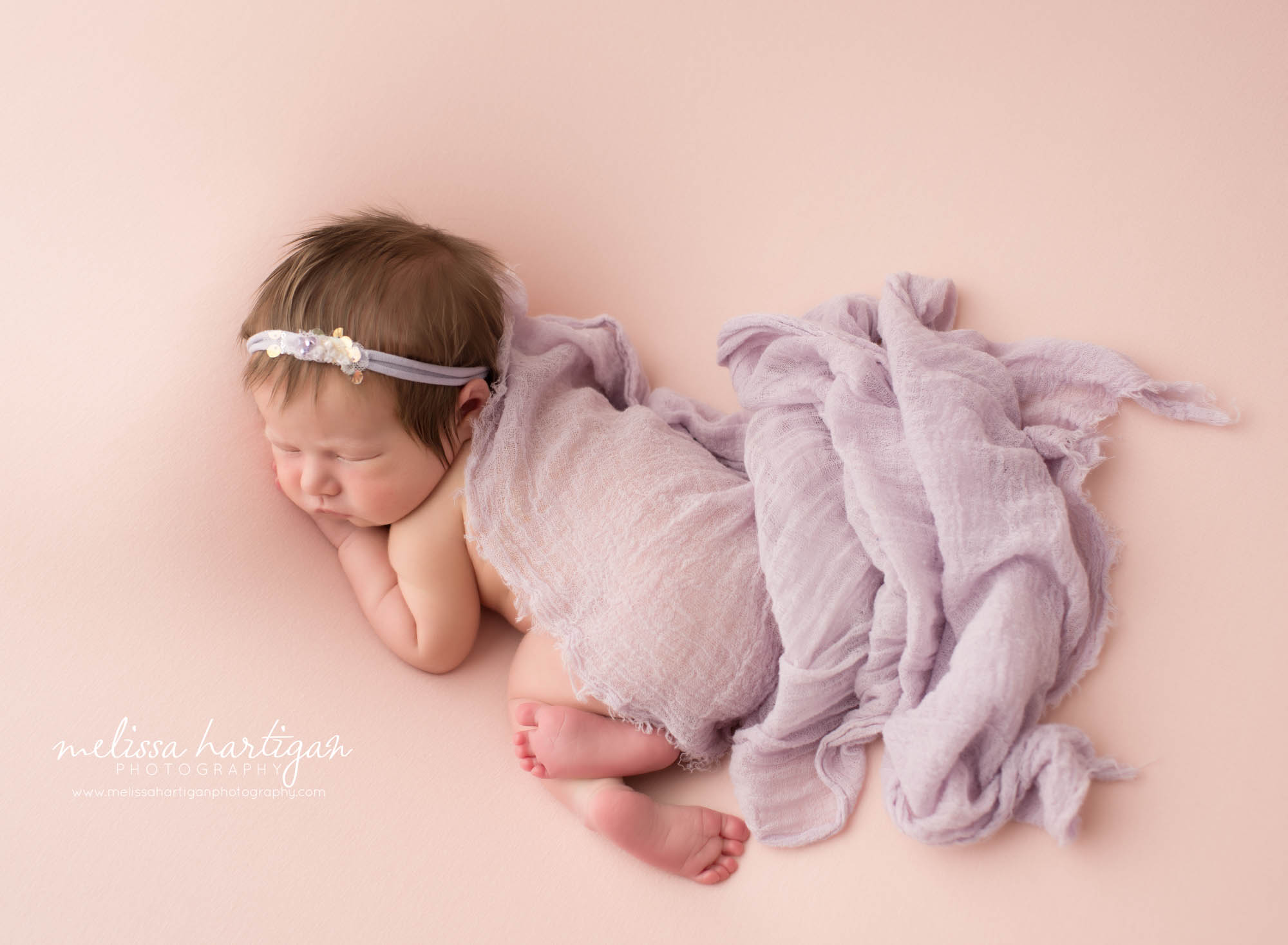 newborn baby girl posed on pink backdrop with purple draping wrap