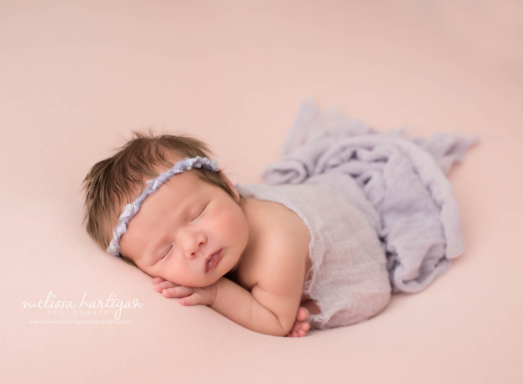 newborn baby girl posed modified taco pose wearing purple headband and purple draping wrap