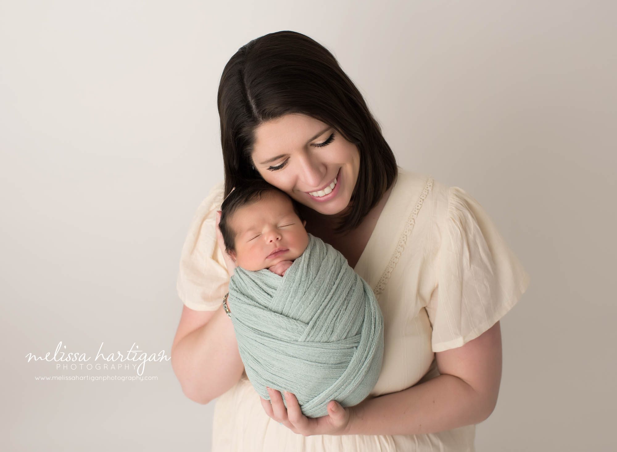 newborn baby boy wrapped in soft teal colored wrap posed with mom parents pose