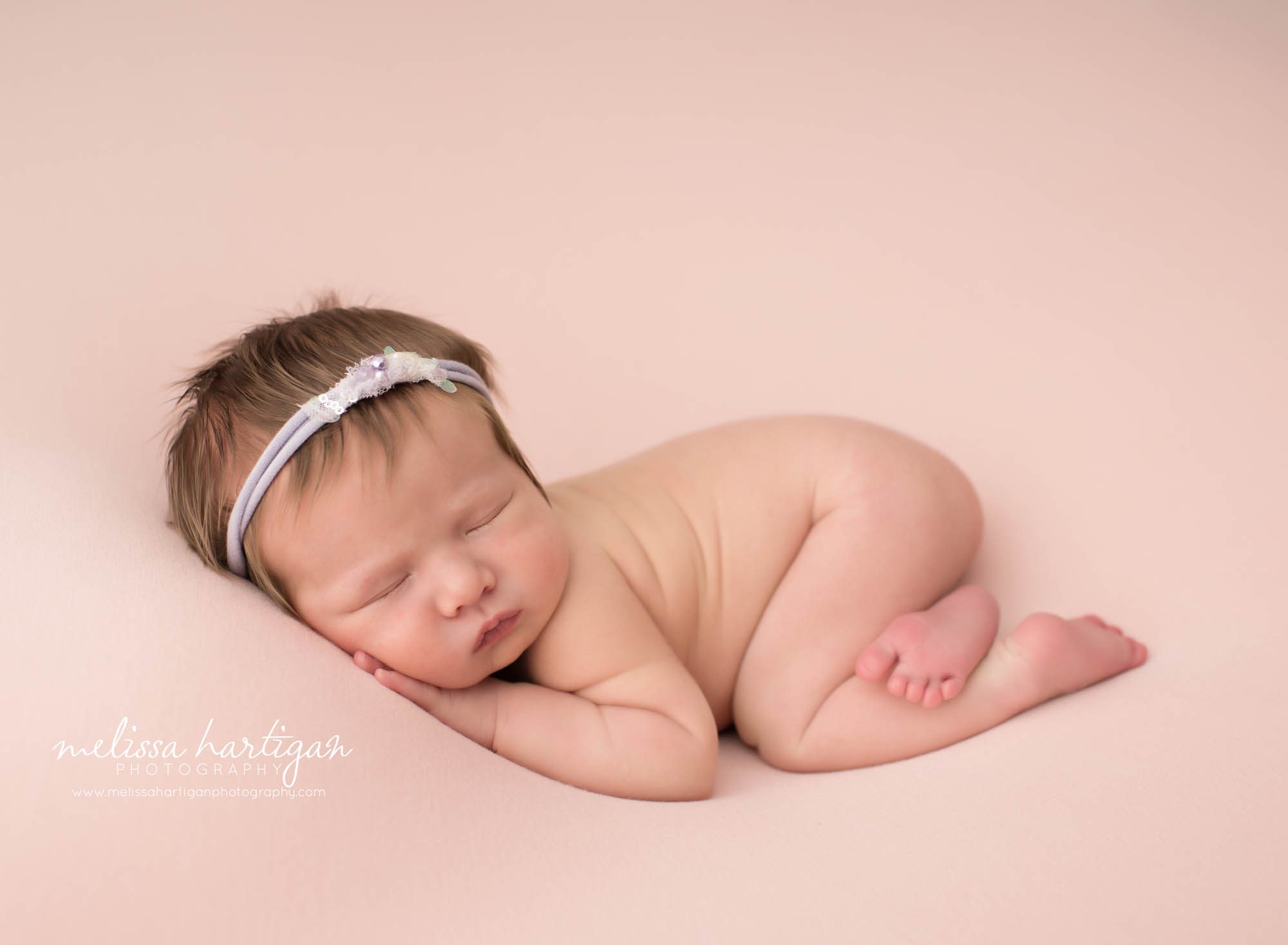 newborn baby girl posed on tummy with hand under cheek wearing purple and cream headband newborn photography tolland