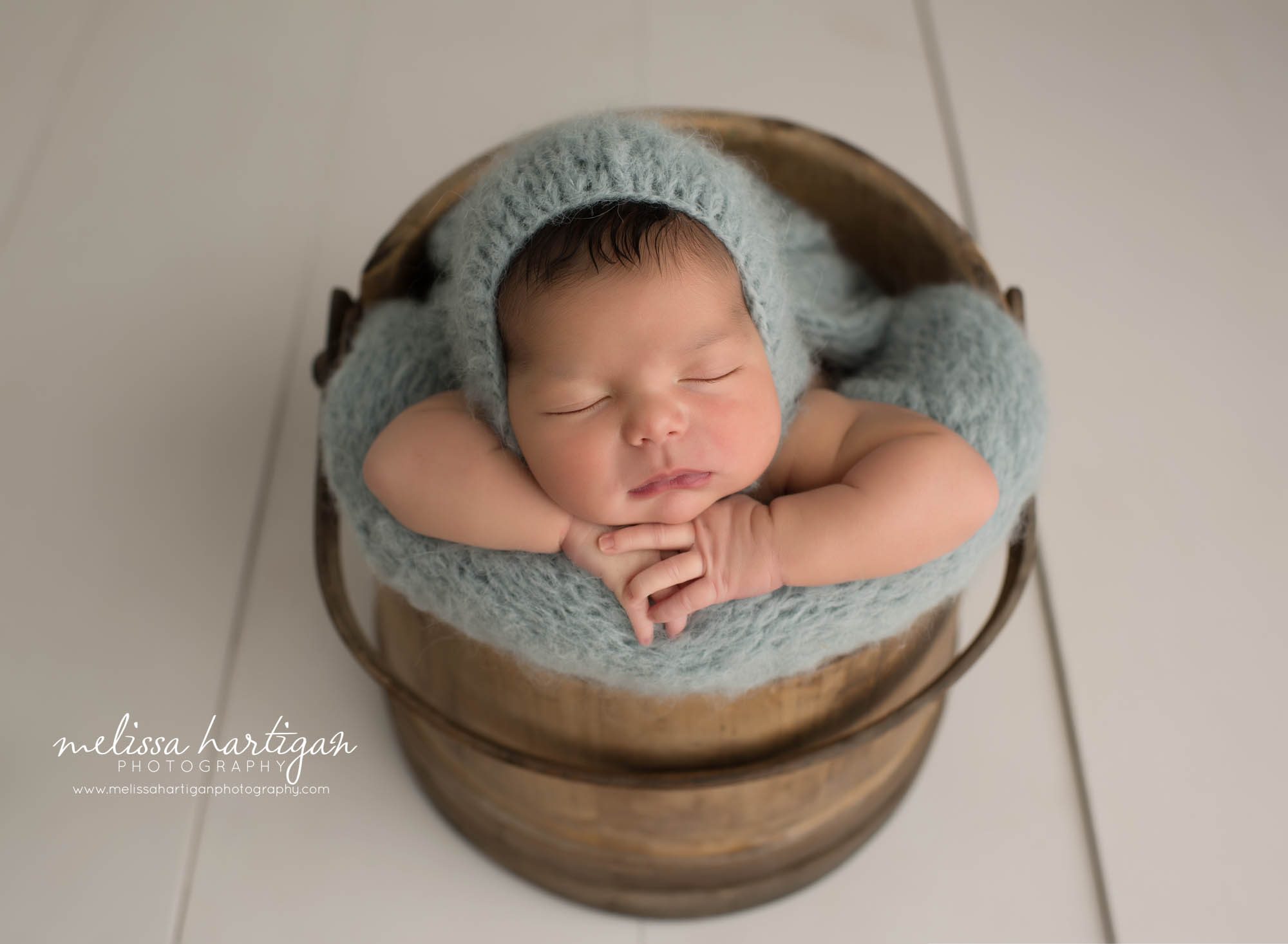 newborn baby boy posed in barrel bucket wearing light teal knitted bonnet newborn photography south windsor CT