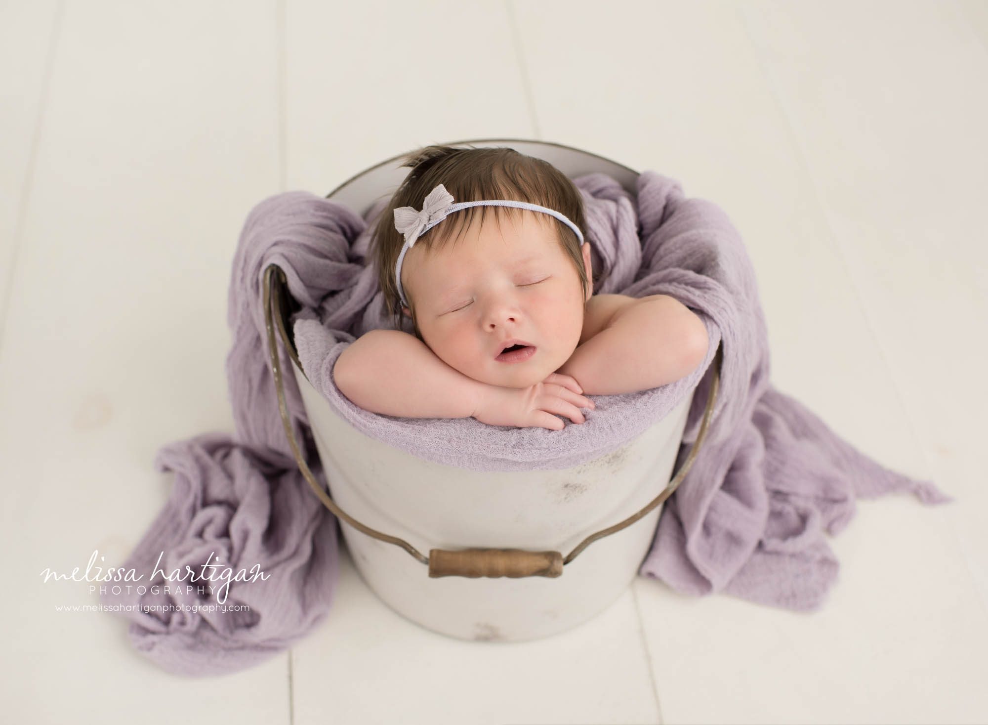 newborn baby girl posed in metal bucket with purple draping wrap