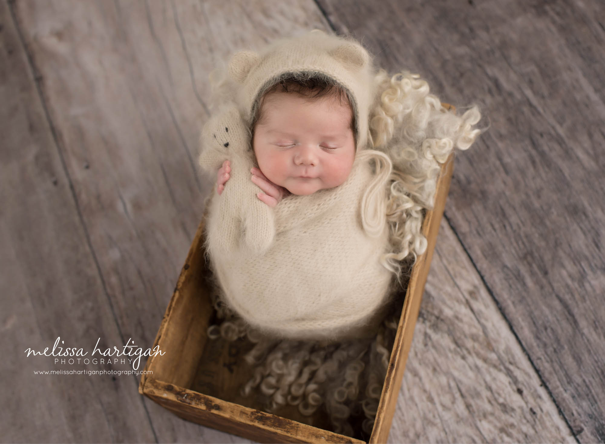 Newborn baby boy wrapped in beige knitted wrap wearing matching bear bonnet and holding matching knitted teddy bear CT newborn photography