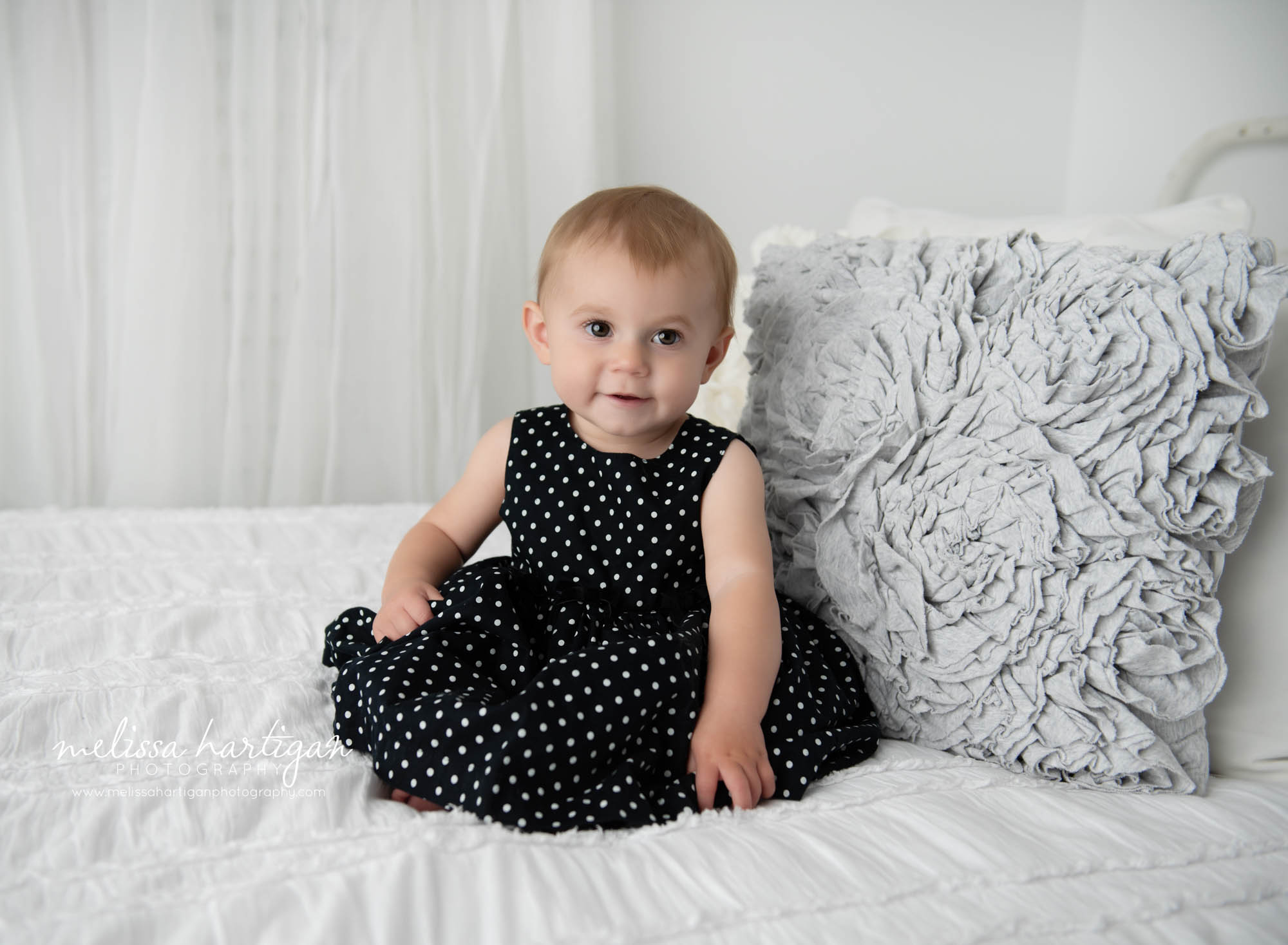 baby girl sitting on bed happy wearing polkadot birthday dress east windsor baby photography