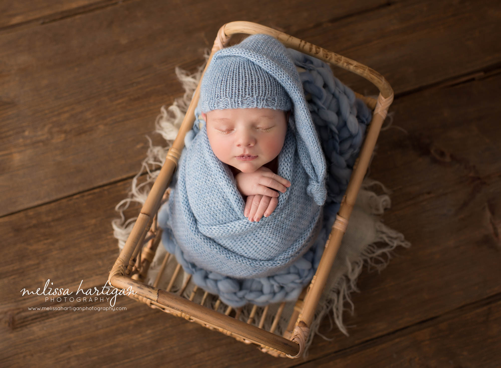 Newborn baby boy wrapped in blue knitted wrap posed in basket