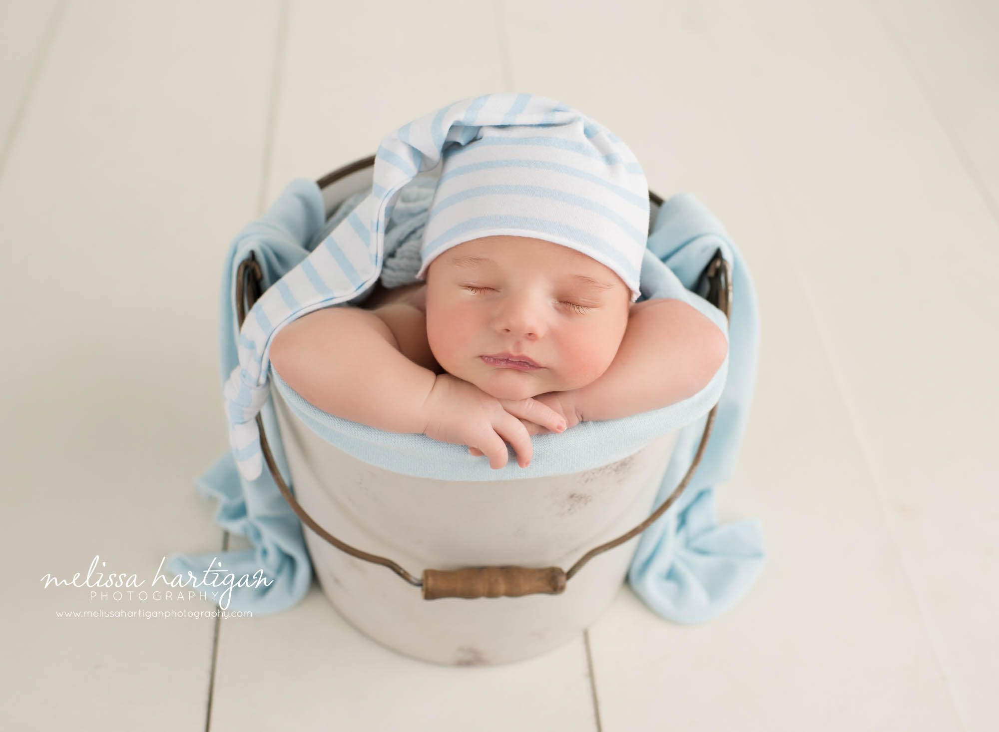 Newborn baby boy posed in metal bucket baby in bucket pose wearing blue and white striped sleepy cap Wethersfield CT Newborn photography