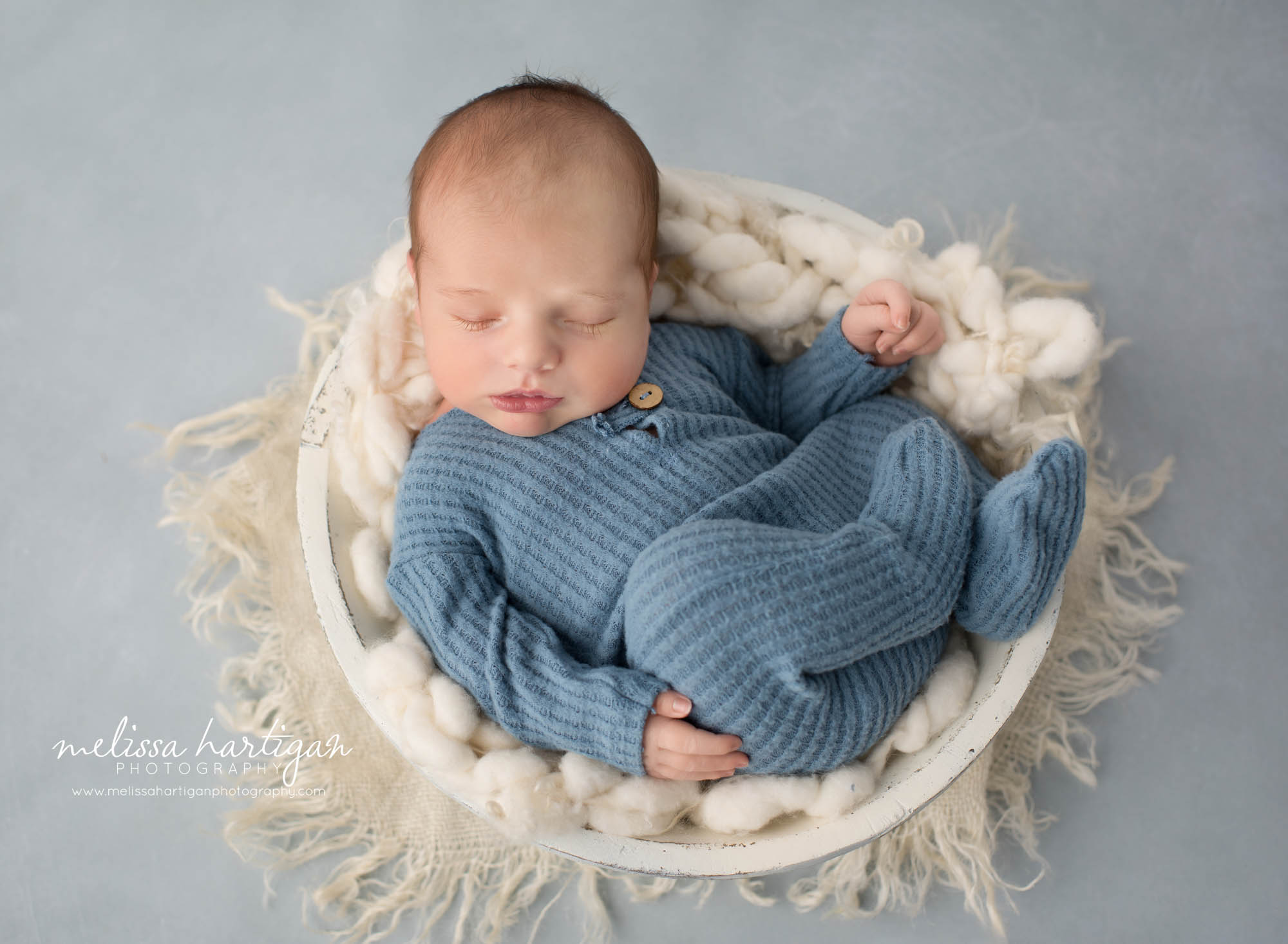 Newborn baby boy posed in wooden bowl with cream layer baby wearing blue waffle knit footed sleeper