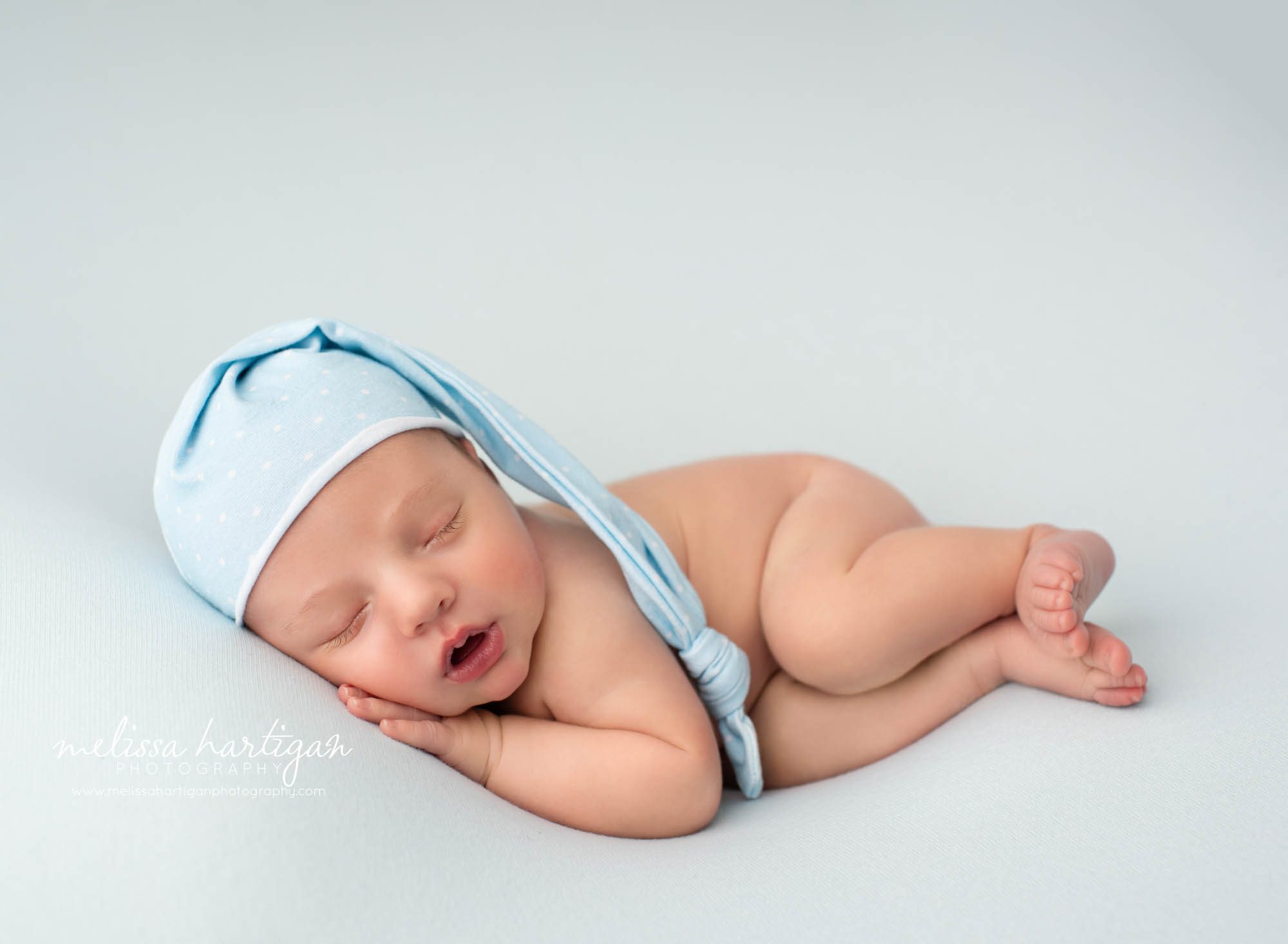 newborn baby boy posed on side wearing sleepy cap