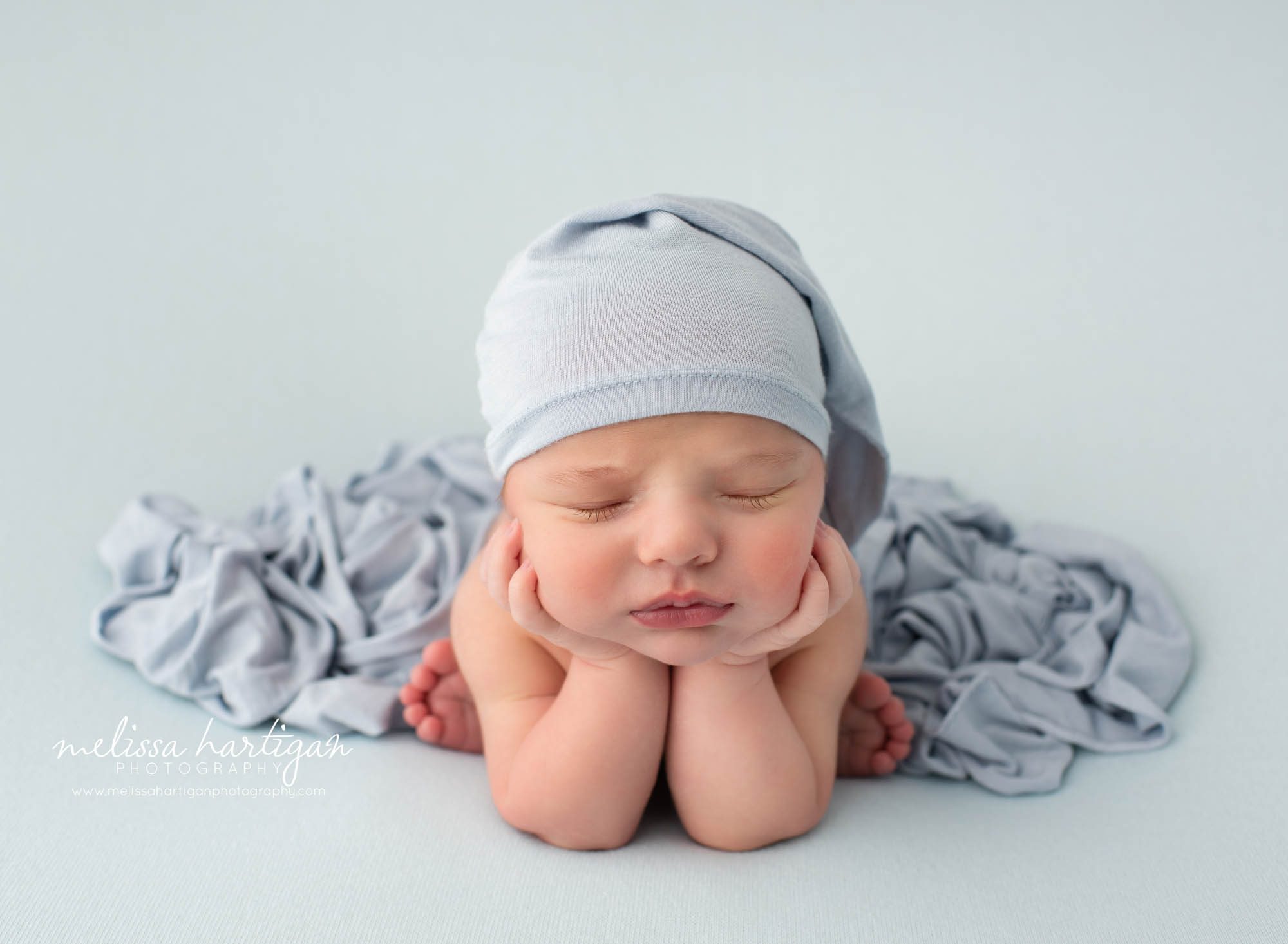 newborn baby boy posed froggy pose wearing blue sleepy cap and blue layer draped over newborn photography Wethersfield CT