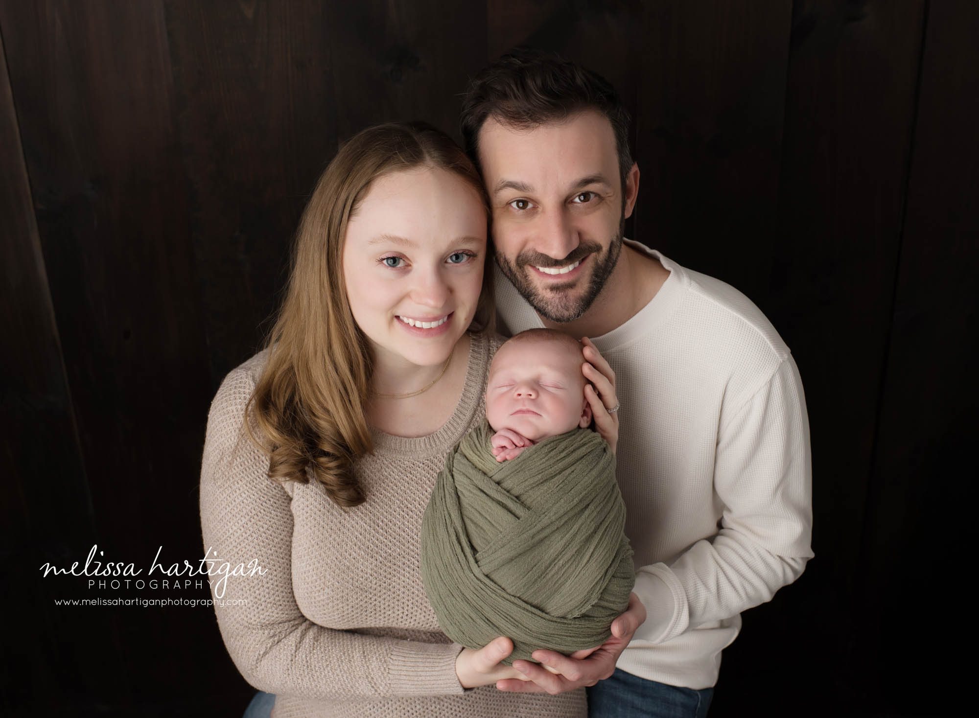 mom and dad holding newborn son smiling happy in newborn photoshoot parents pose