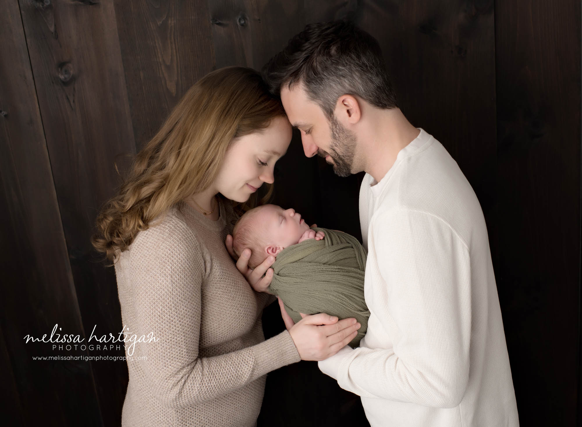 mom and dad standing forehead to forehead holding newborn son
