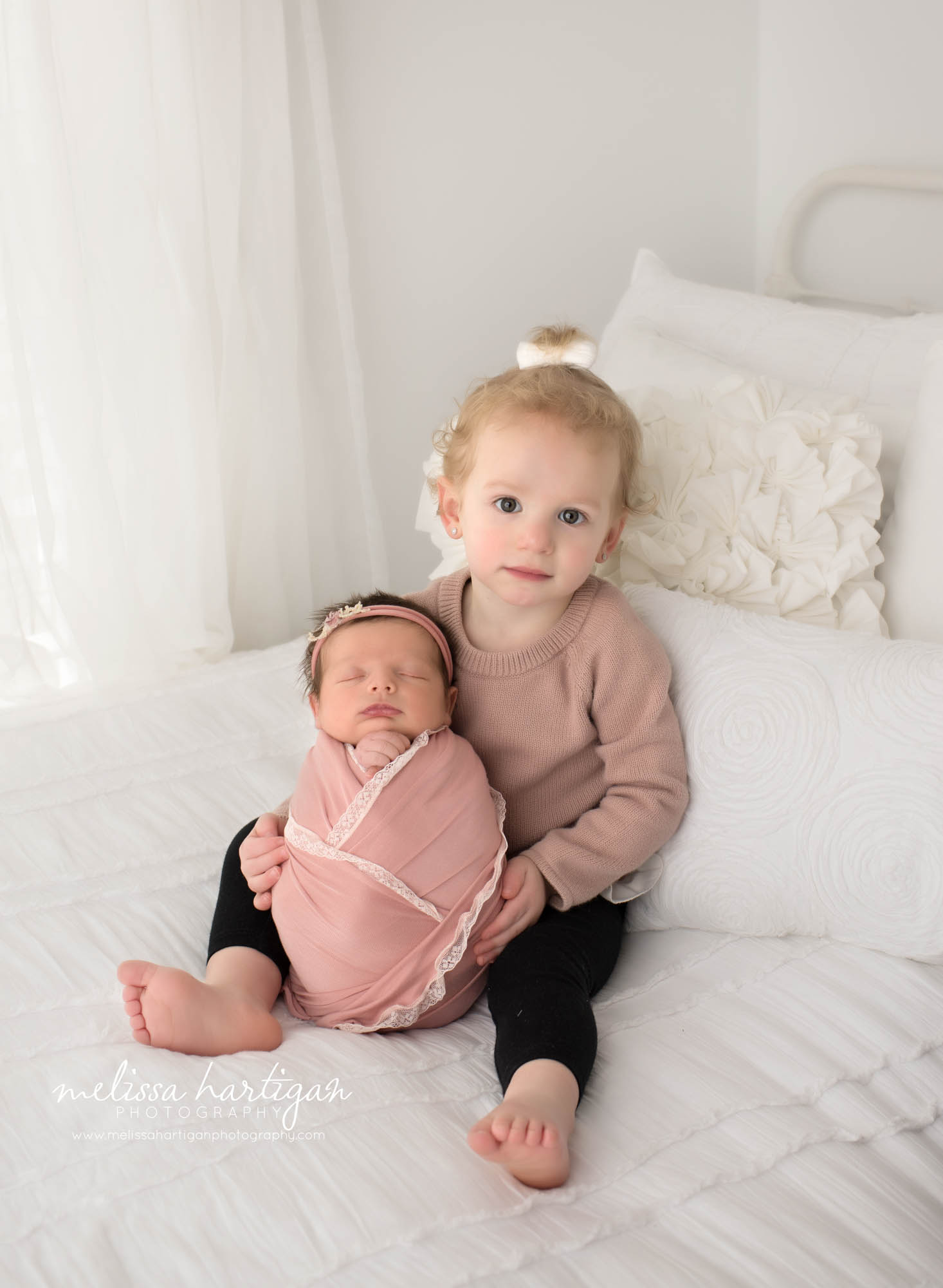 big sister sitting on bed holding newborn baby sister