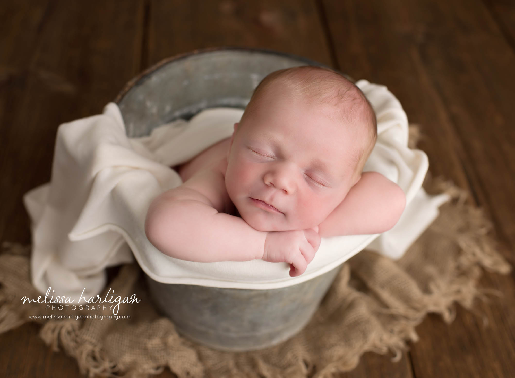 newborn baby boy posed in bucket with cream draping wrap
