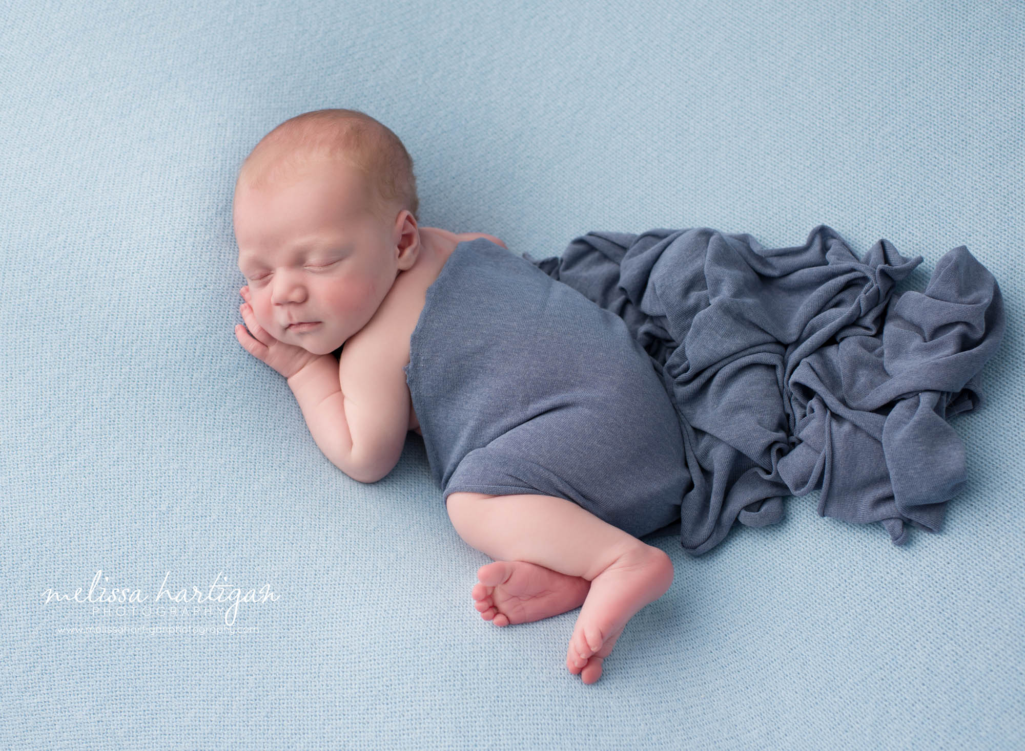 newborn baby boy posed on blue backdrop with darker blue layer over him