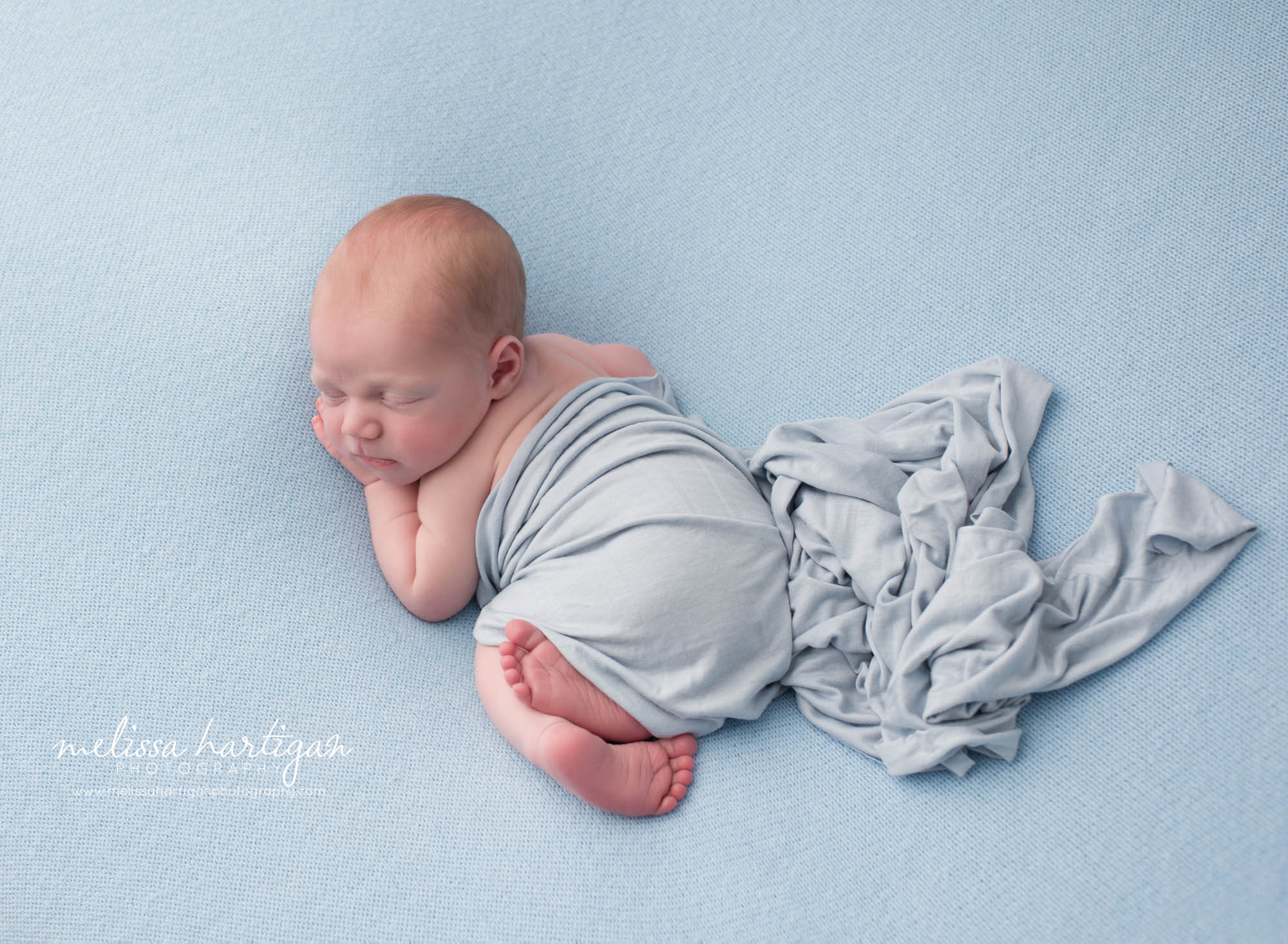 newborn baby boy posed on light blue backdrop with light blue layer draped over him hebron newborn photography