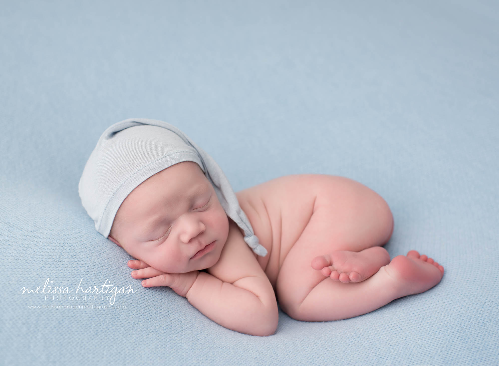 newborn baby boy posed on tummy wearing light blue sleepy cap tolland county newborn photography photoshoot