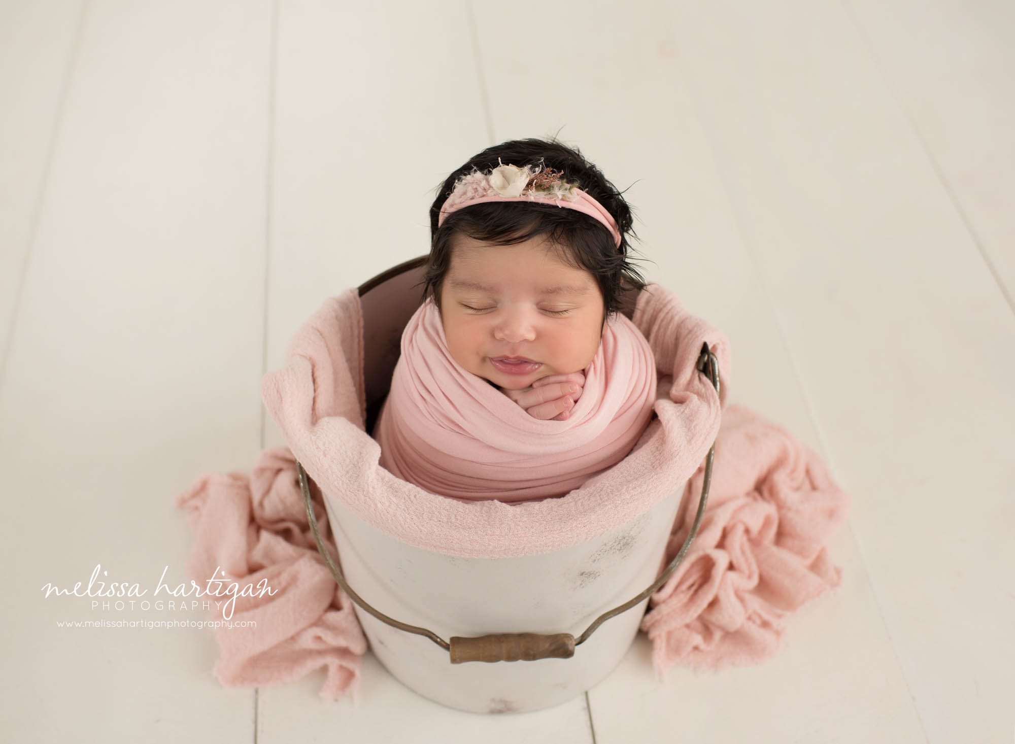 newborn baby girl posed in bucket in pink wrap wearing pink floral headband Suffield CT Newborn photography