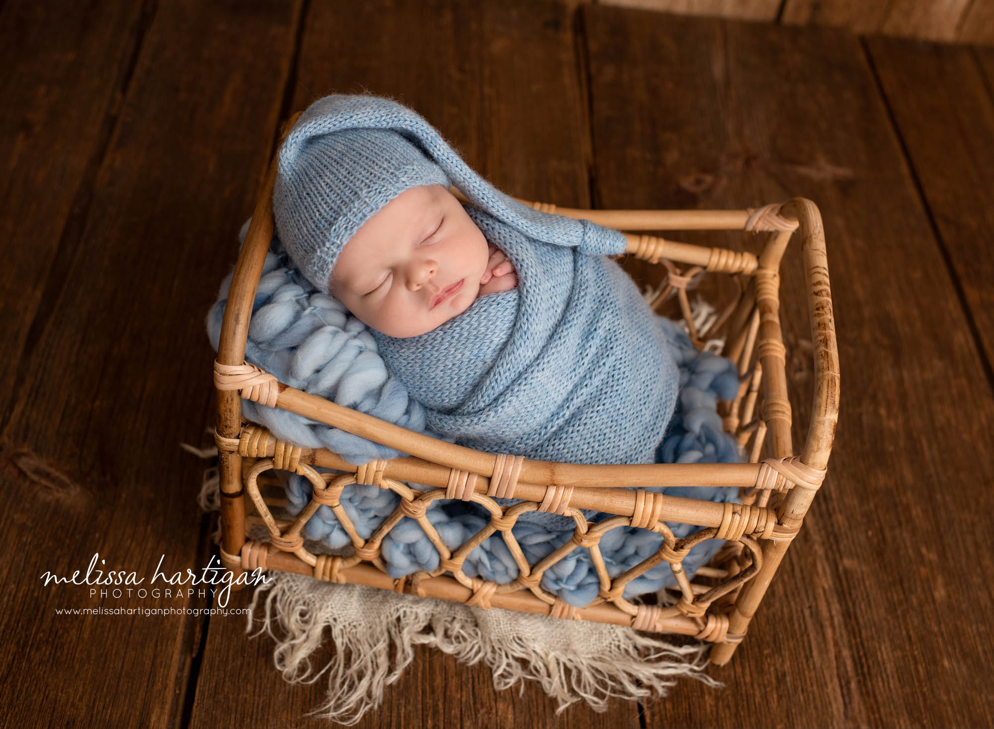 newborn baby boy posed in basket wrapped in knitted blue wrap wearing knitted blue sleepy cap Newborn Photography Windsor CT