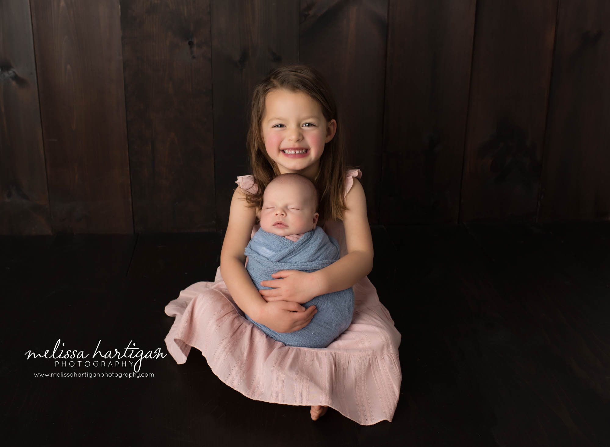 Big sister holding newborn baby brother wrapped in blue wrap