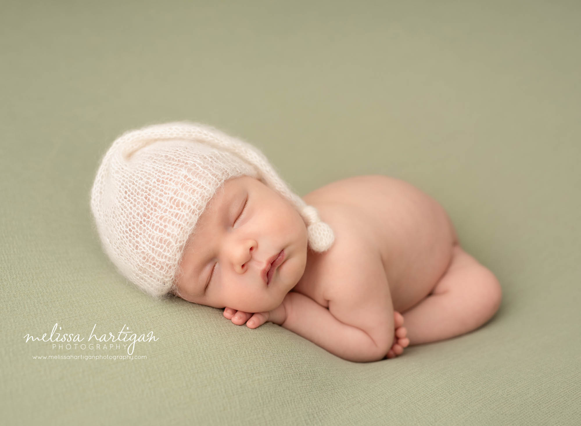 newborn baby boy posed on sage green backdrop wearing cream knitted wrap