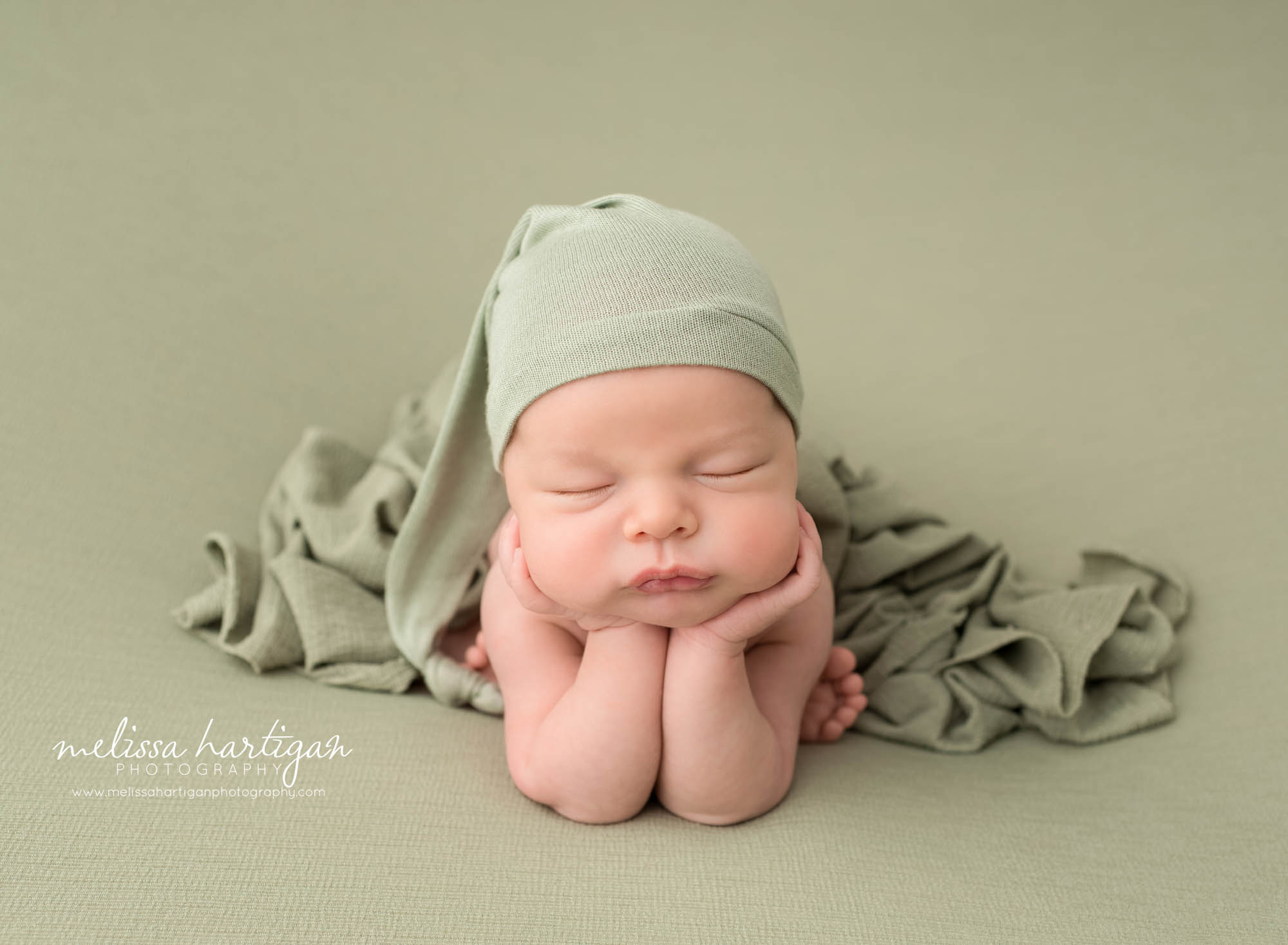 newborn baby boy posed froggy pose wearing sage green sleepy cap draped with sage green layer Newborn Photography Windsor CT