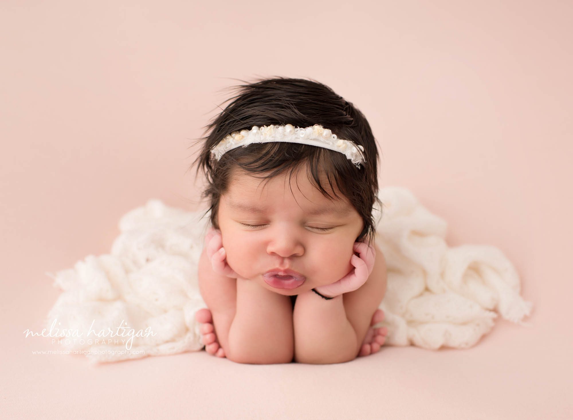 newborn baby girl posed froggy pose wearing cream headband and cream layer draped over her back Suffield CT Newborn photography