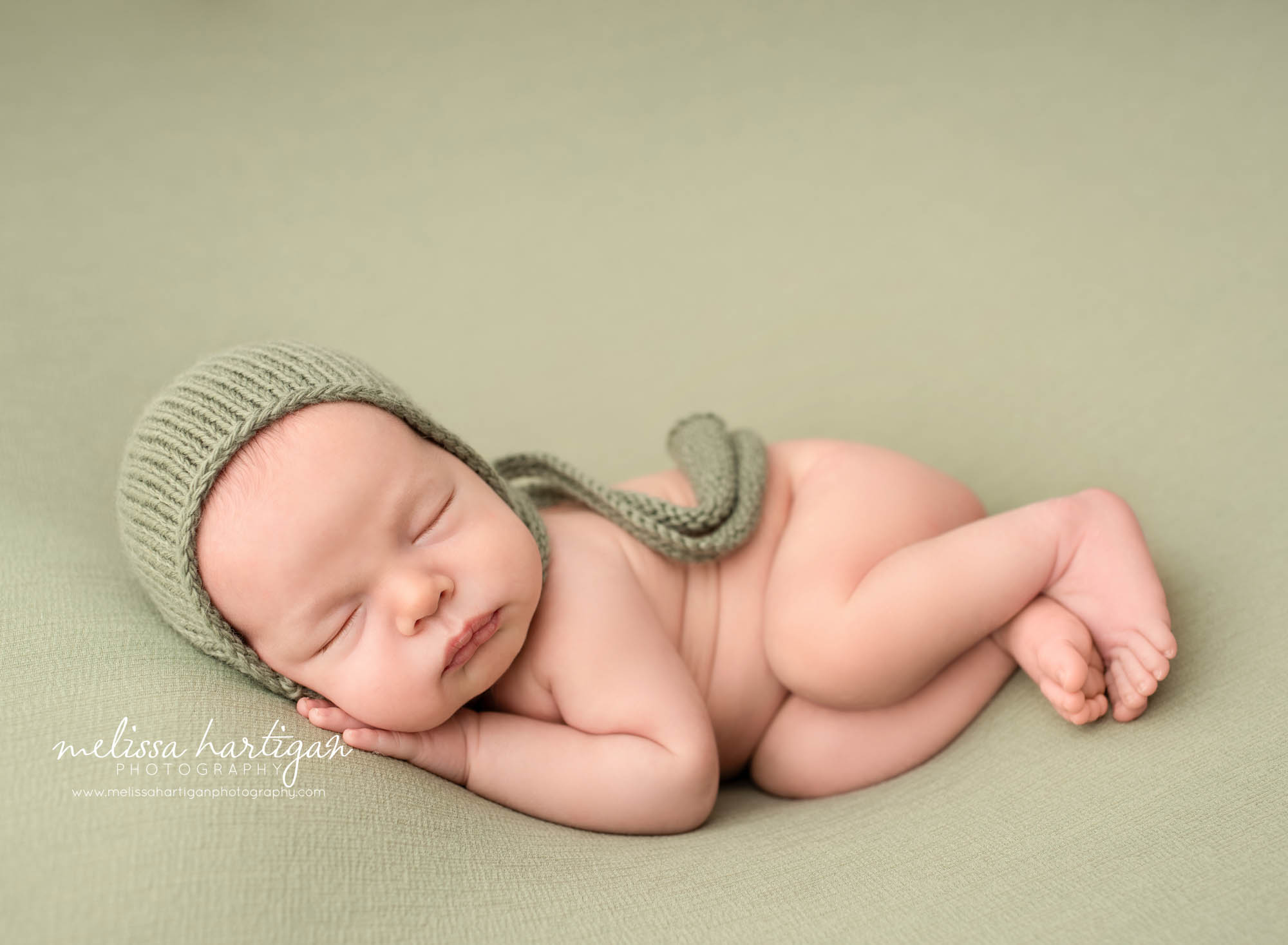 newborn baby boy posed on side wearing green bonnet