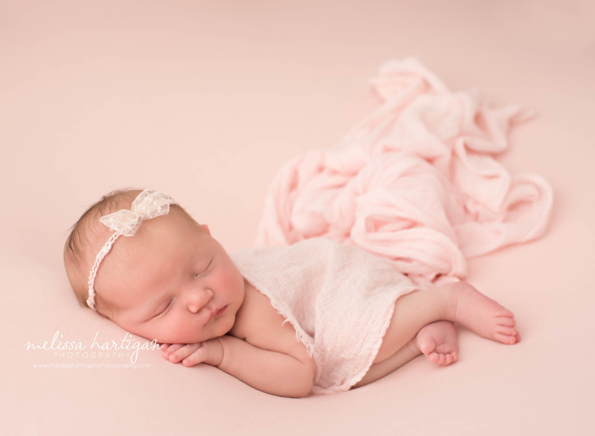 newborn baby girl posed on side wearing bow headband and pink layer draped over her East Haddam CT Baby Photography