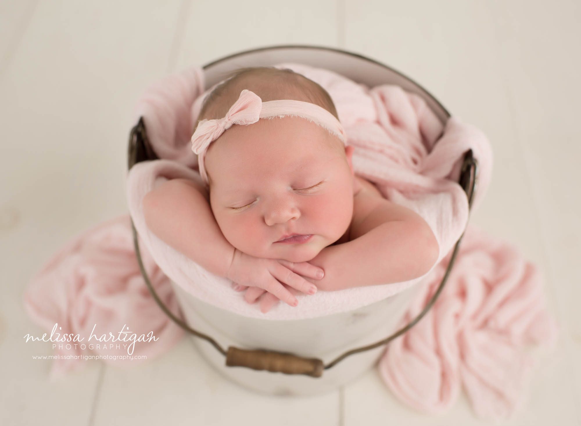 newborn baby girl pose din bucket wearing pink bow headband
