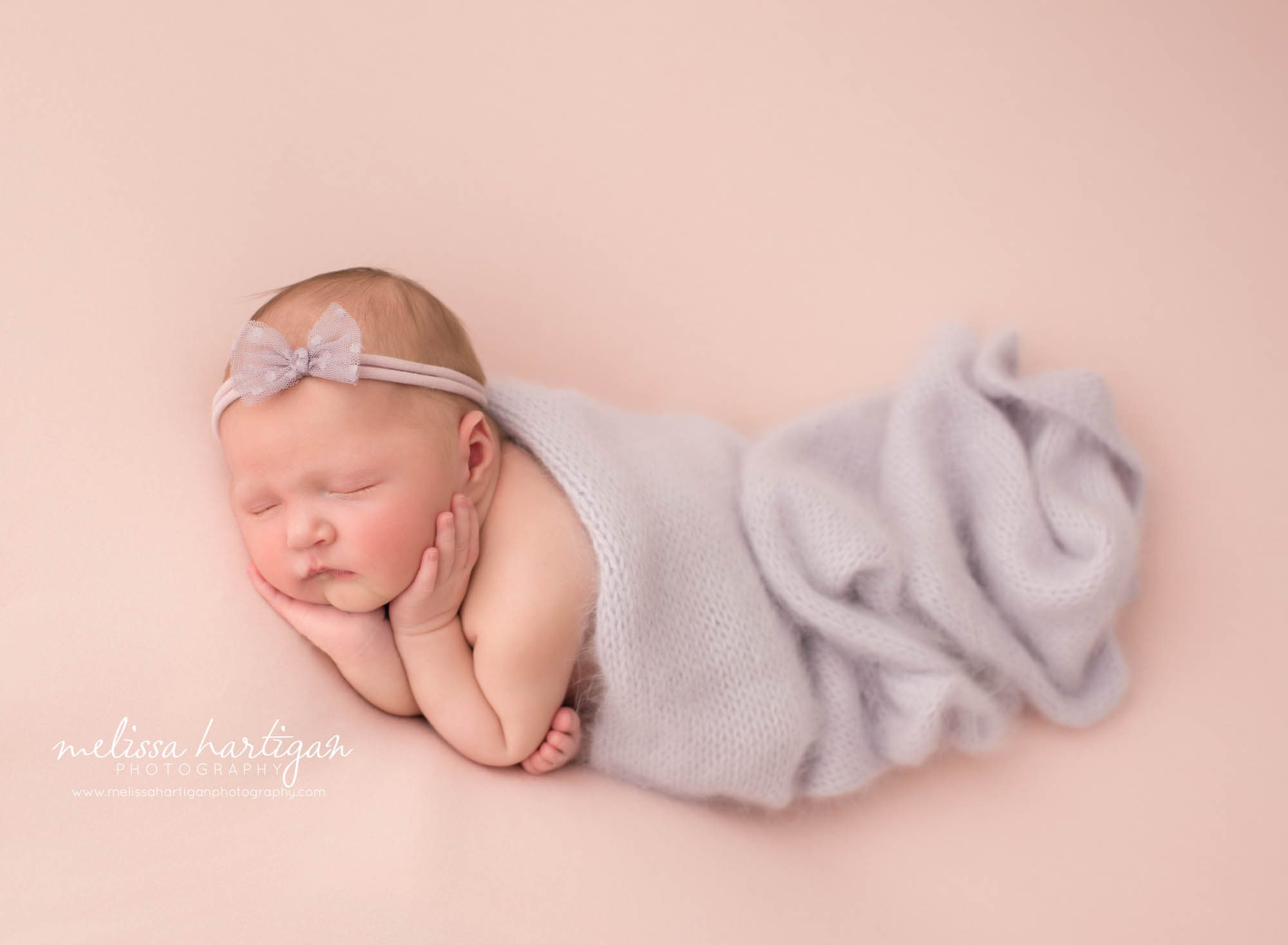 newborn baby girl posed on side wearing purple bow headband and purple knitted layer draped over her East Haddam CT Baby Photography