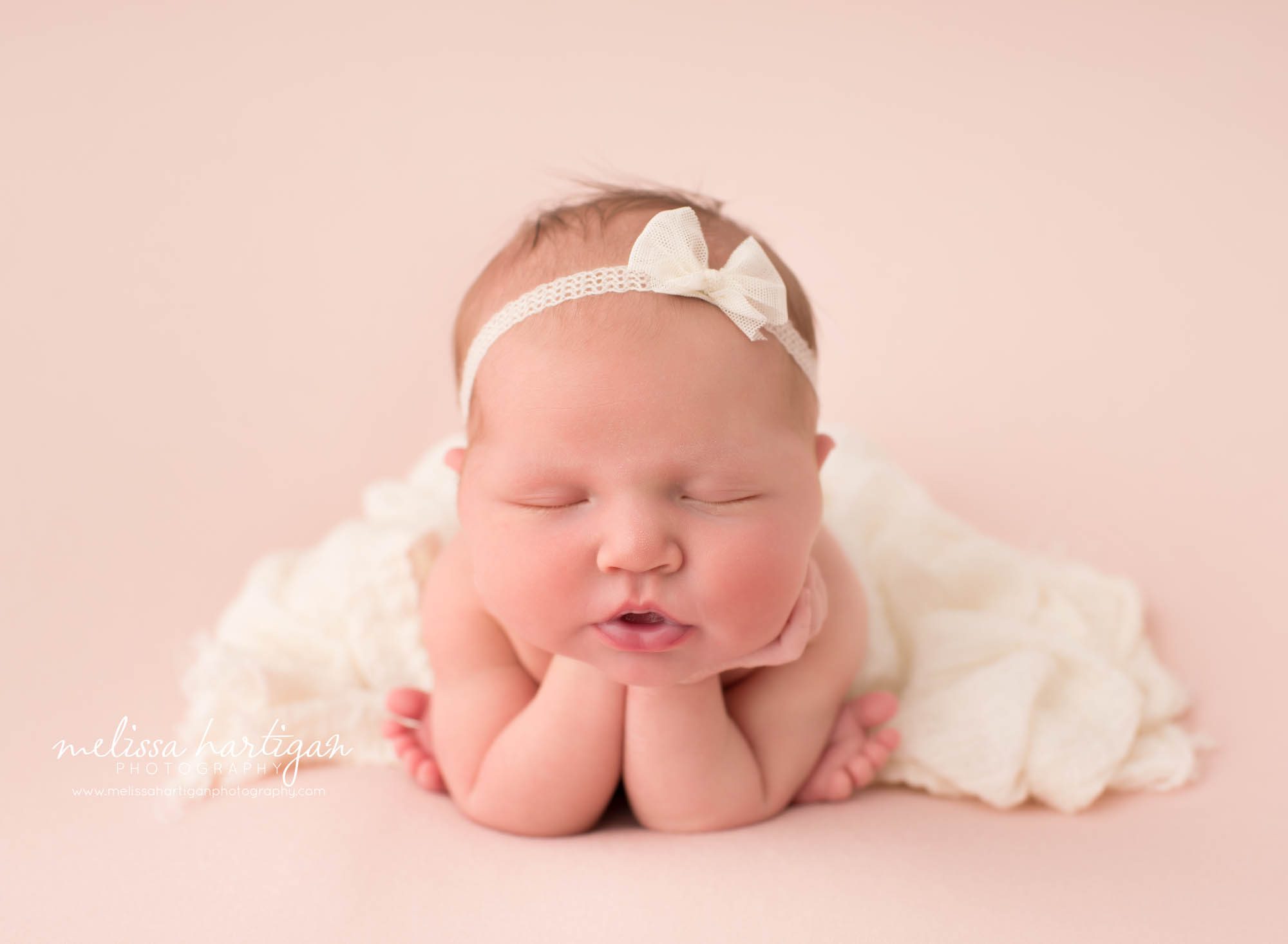 newborn baby girl posed froggy pose wearing cream bow headband