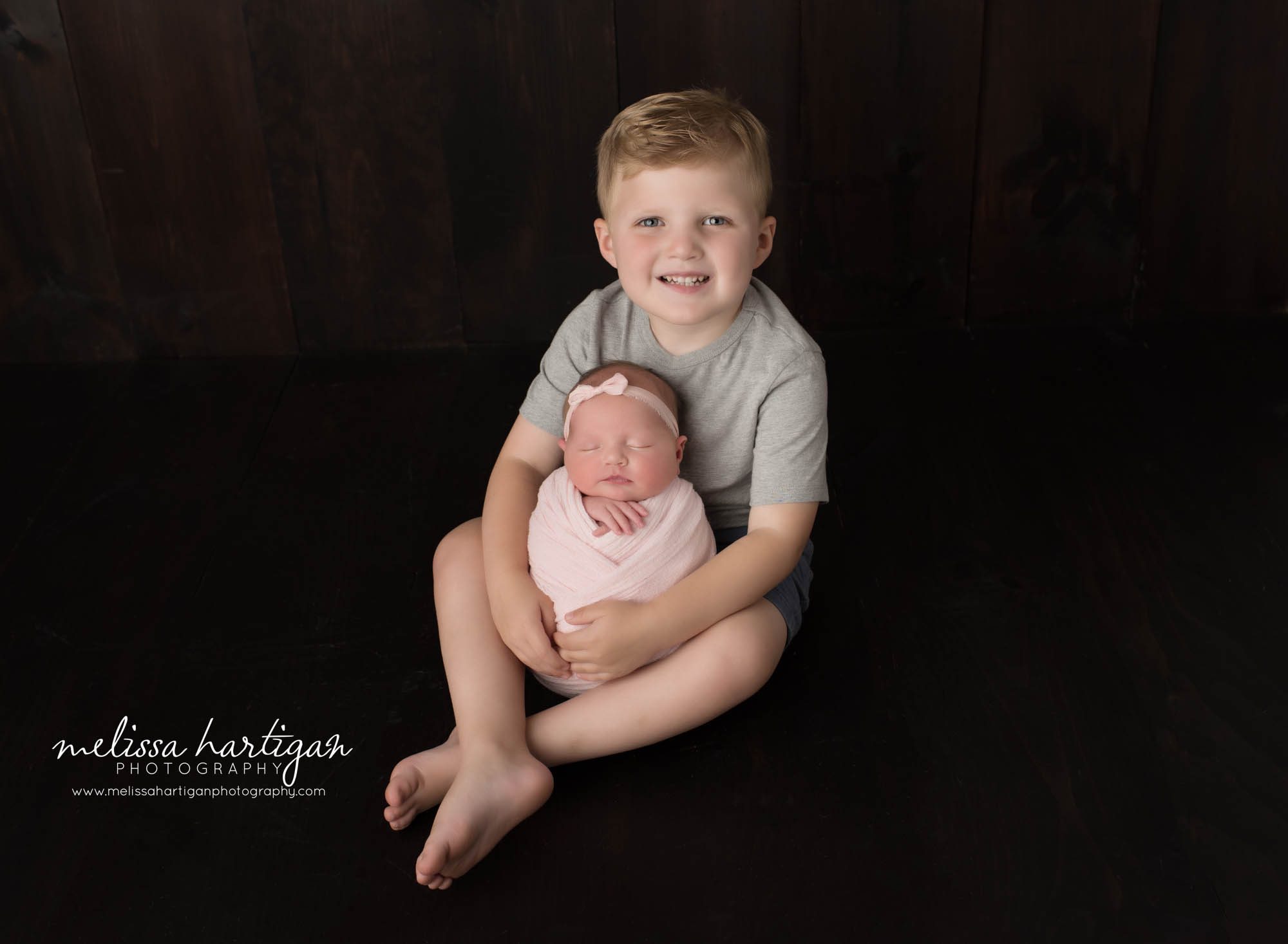 big brother smiling holding newborn baby sister sibling pose newborn photoshoot