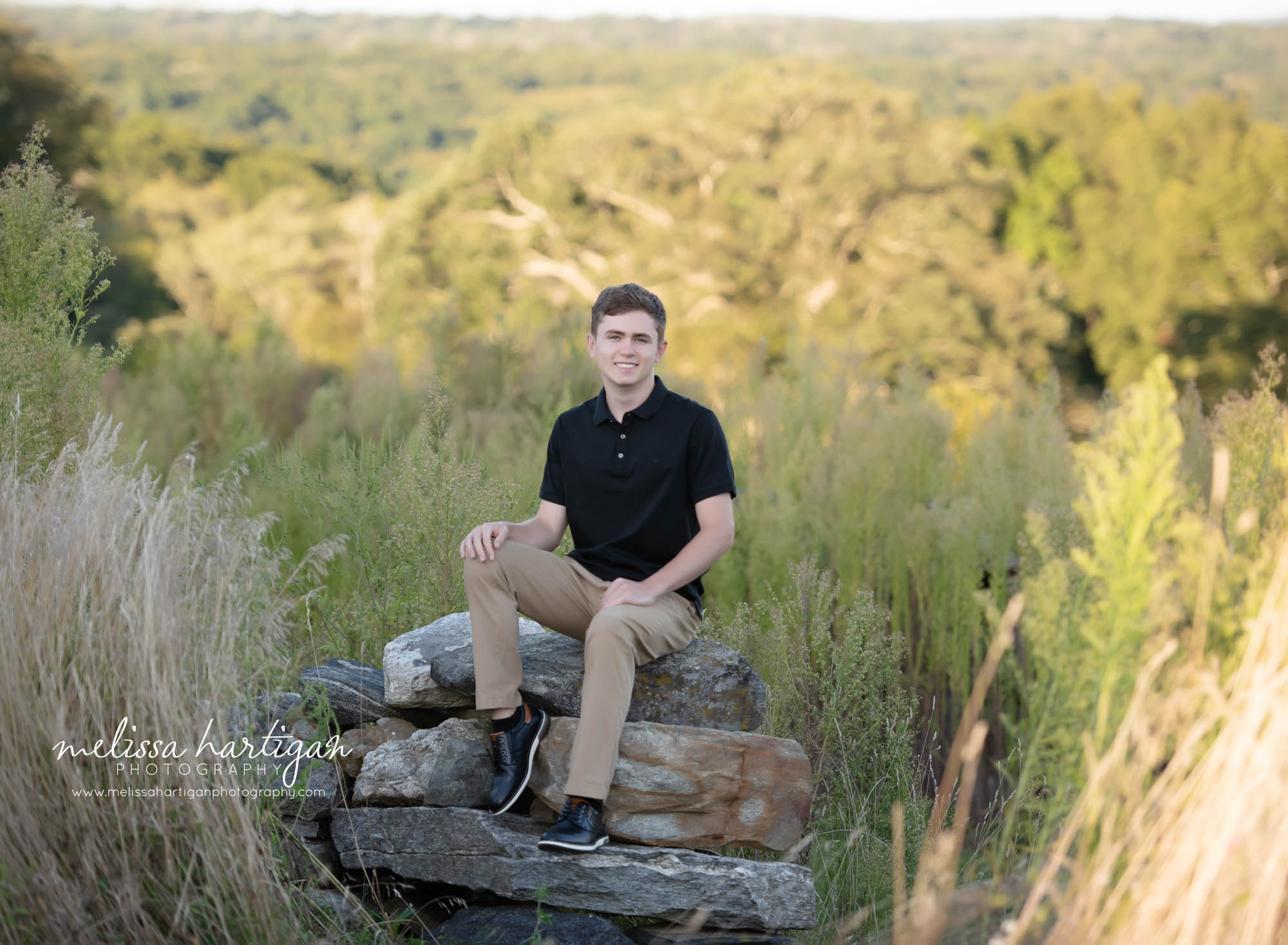 Teenager sitting on rock in park smiling happy