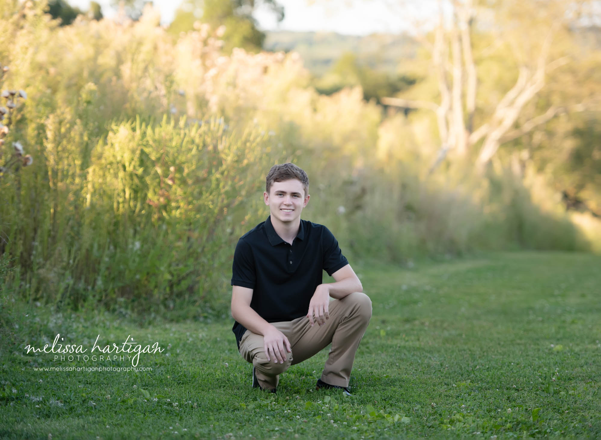 High school senior kneeling down in the grass smiling for senior portrait photoshoot Senior Photography Chesire CT