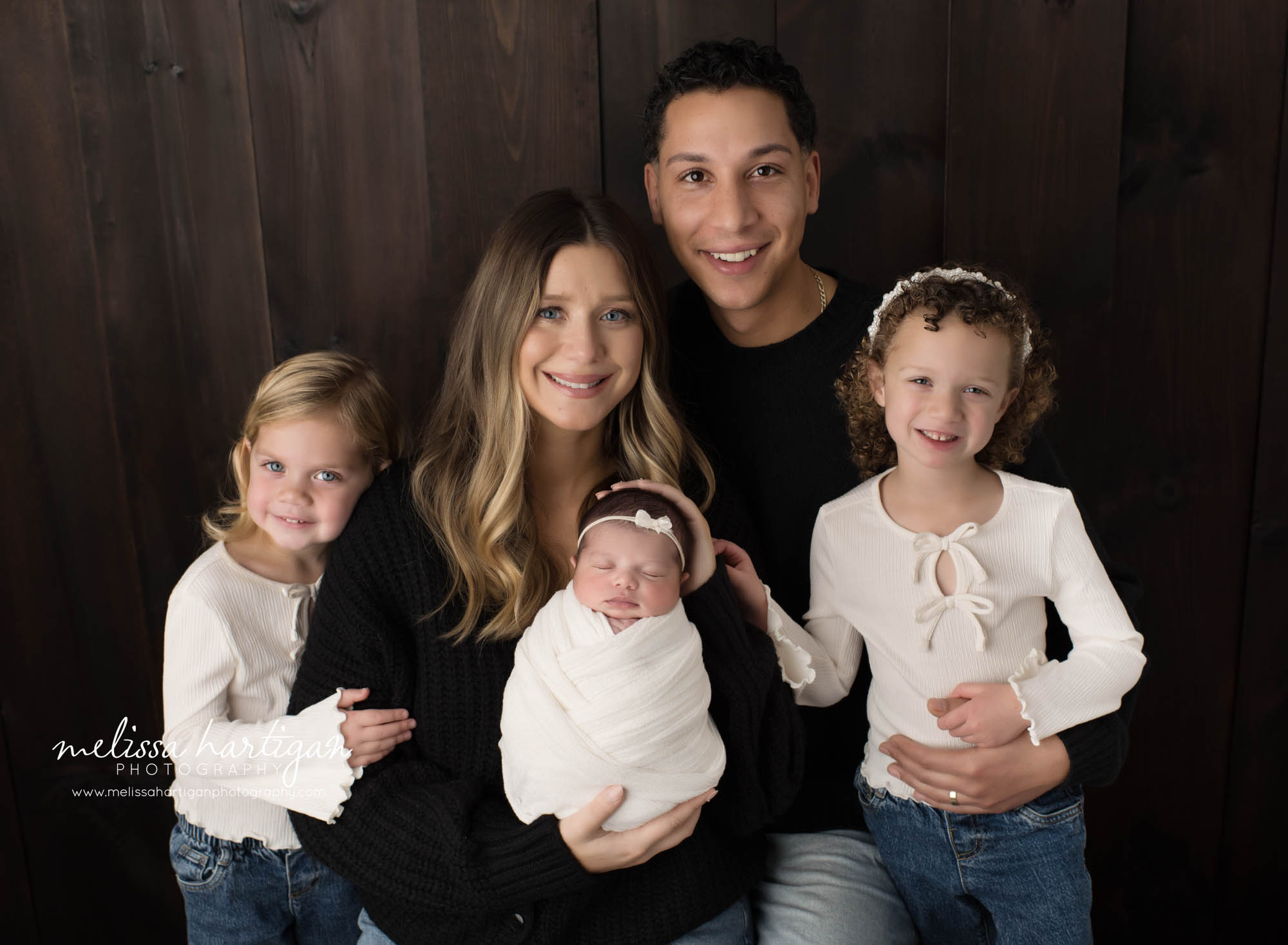 Mom dad twin big sisters and newborn baby girl posed together for family pose