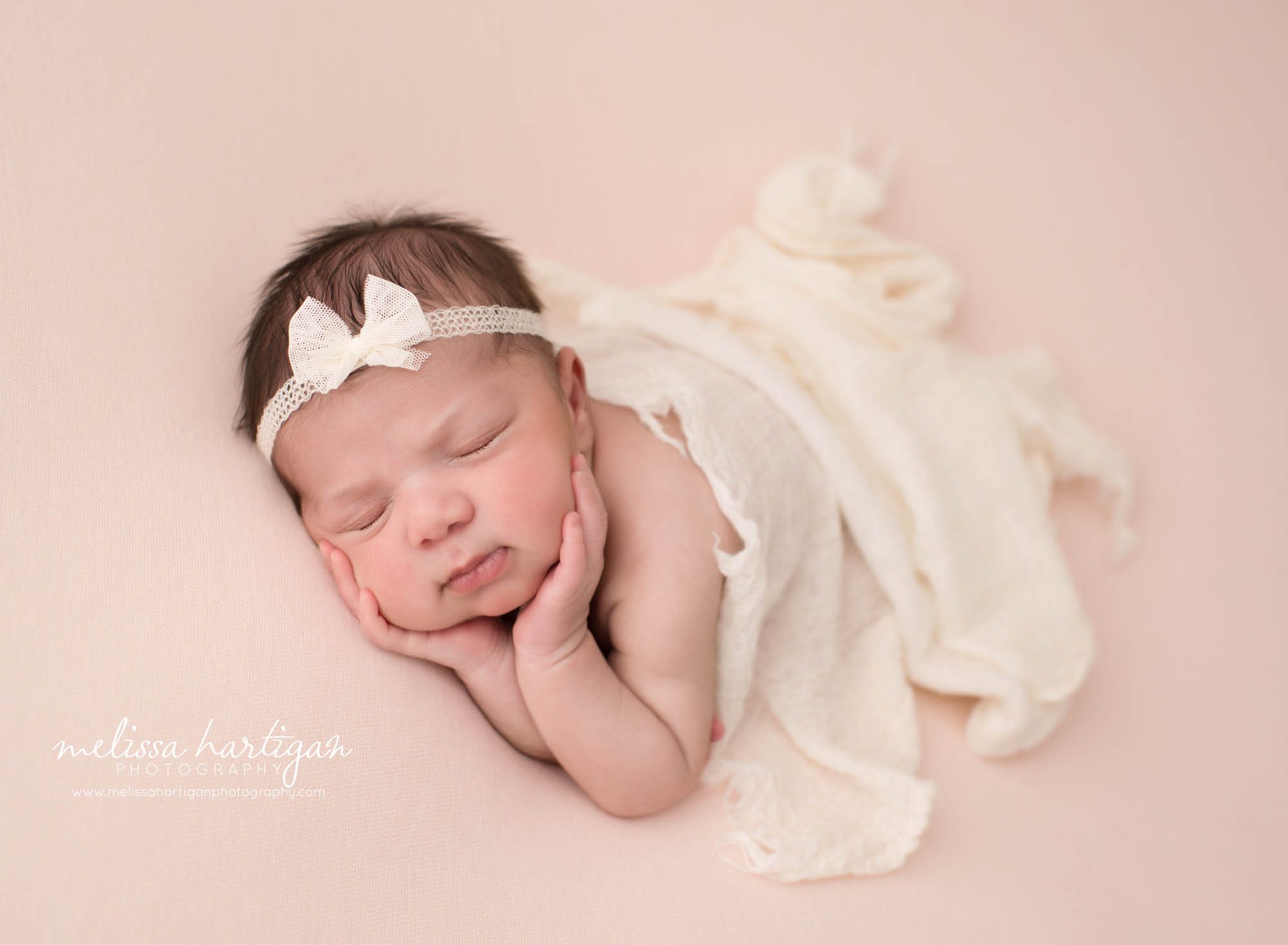 Newborn baby girl posed on light pink backdrop with white bow headband Newborn Photography West Hartford