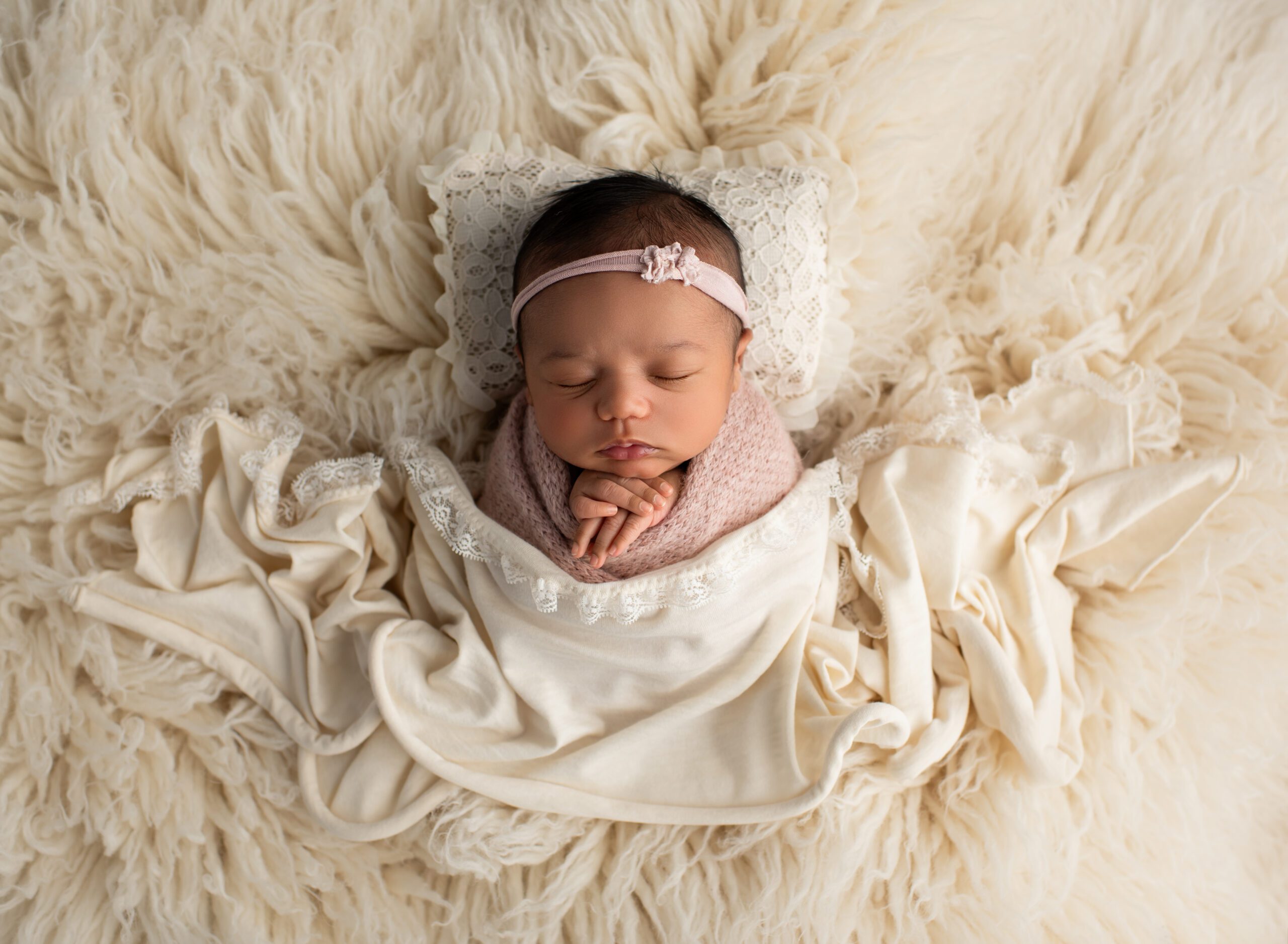 Newborn baby girl posed on crema flokati wearing pink headband Newborn Photography Simsbury CT