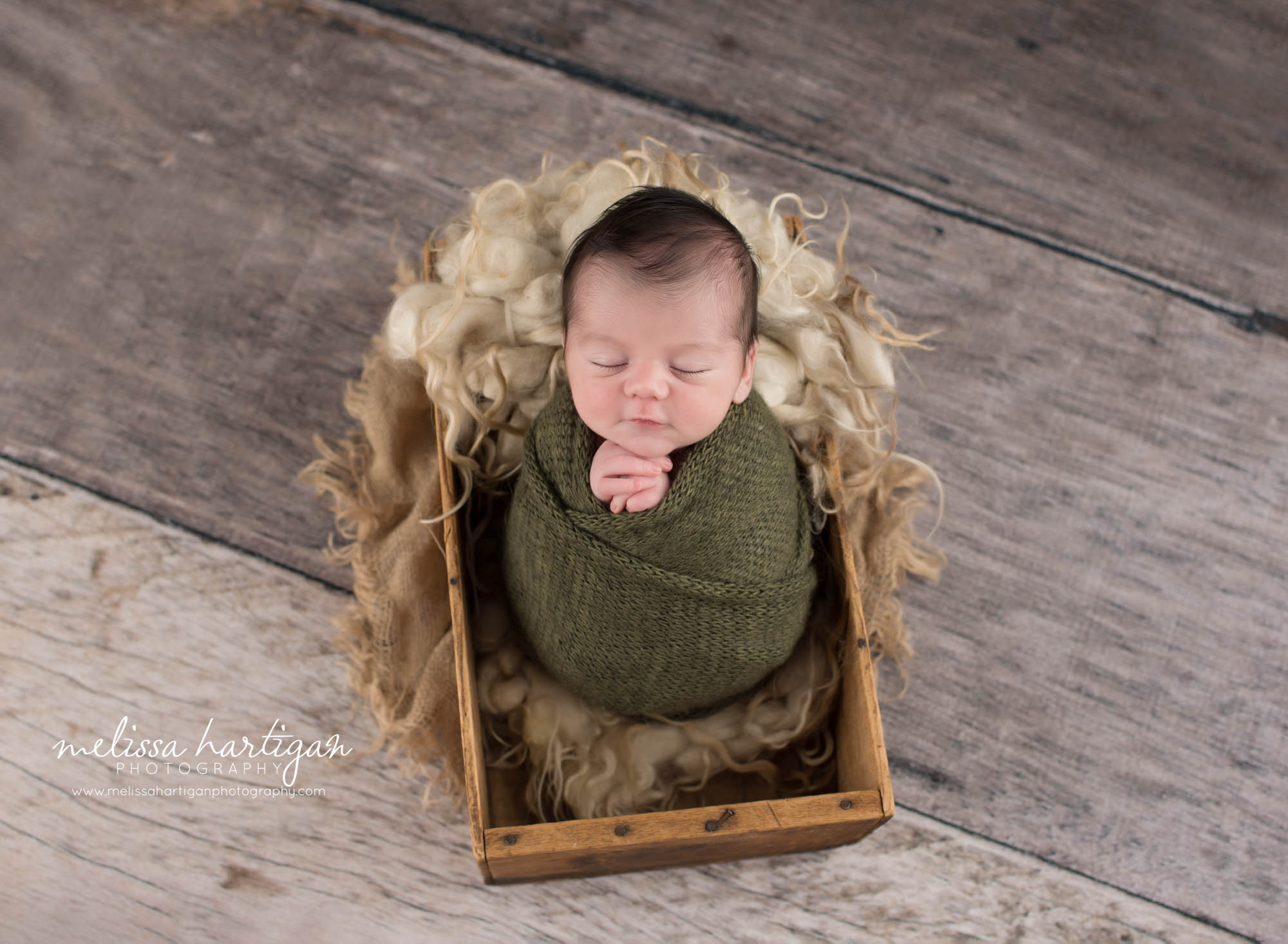 Newborn baby boy posed swaddled in a green wrap posed in a wooden crate